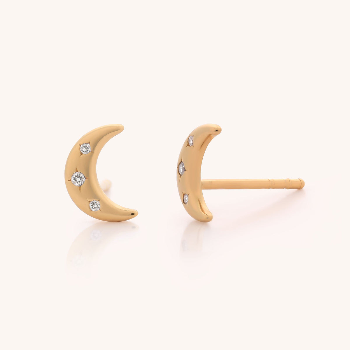 The Starlit Moon Stud Earrings feature a pair of delicately shaped gold crescent moons, each adorned with three sparkling cubic zirconia studs, beautifully displayed against a light background.