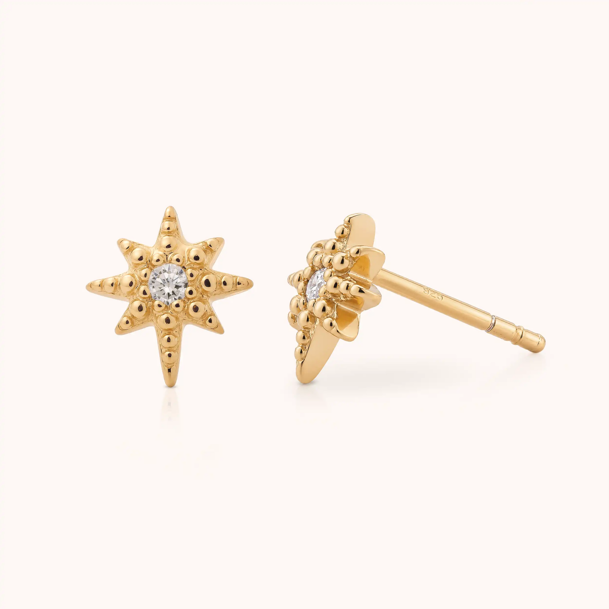 The Celestial Star Stud Earrings are gold-plated and feature elegant eight-pointed stars, each adorned with a small clear gemstone at the center, displayed on a light background.