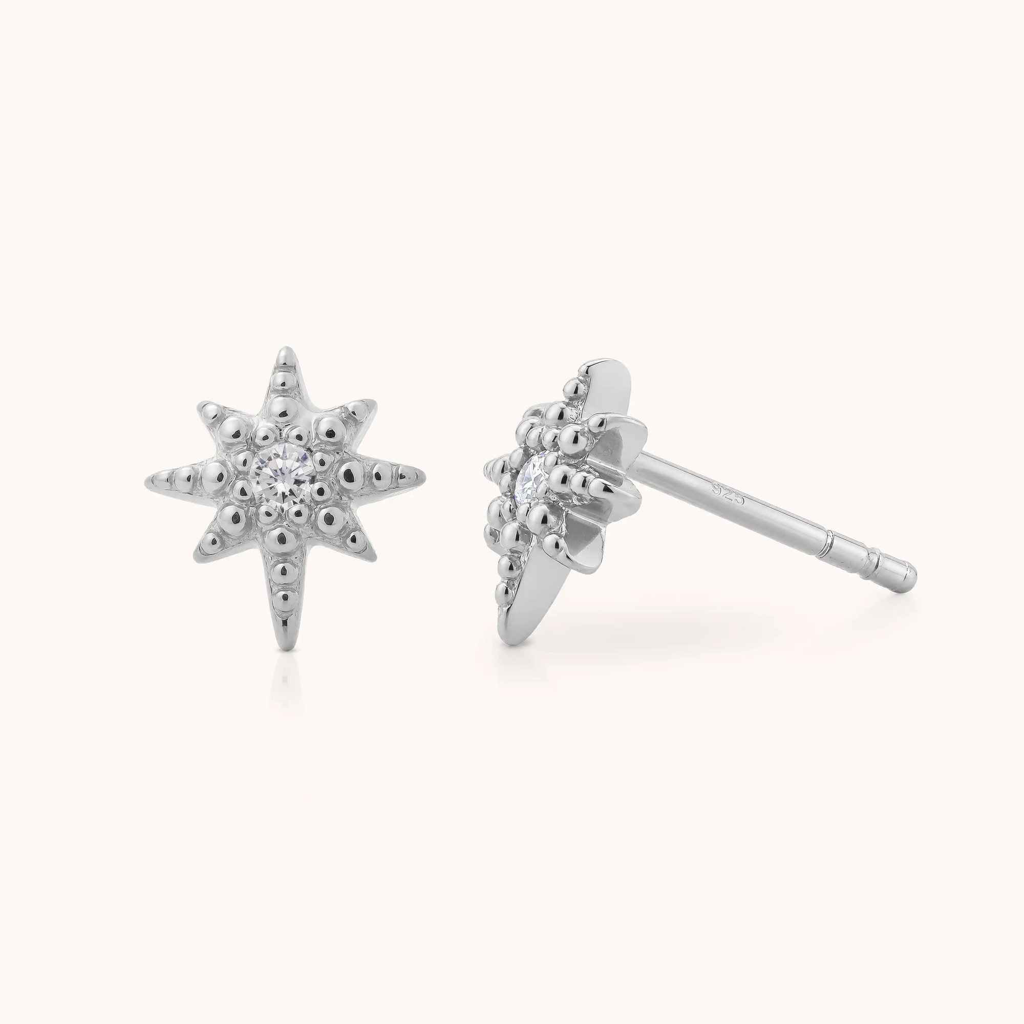 The Celestial Star Stud Earrings are a pair of sterling silver studs, each adorned with a small central gemstone and textured detailing on the star points, showcased against a simple light background.