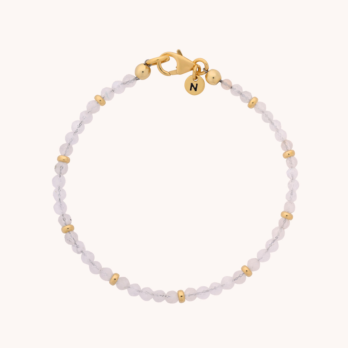 Introducing the Rainbow Moonstone Orbit Bracelet - June: a delicate, handcrafted bracelet featuring clear round rainbow moonstone beads paired with small gold spacers. Finished with a gold clasp and a charming round initial “N” charm, this elegant piece makes a thoughtful June birthstone gift or a lovely personal accessory.