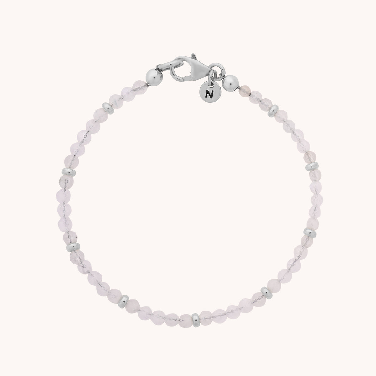 Introducing the Rainbow Moonstone Orbit Bracelet - June: a delicate handcrafted bracelet featuring small, round pale pink moonstone beads separated by tiny silver accents, finished with a silver clasp and a petite charm engraved with the letter N—an elegant piece celebrating the June birthstone.