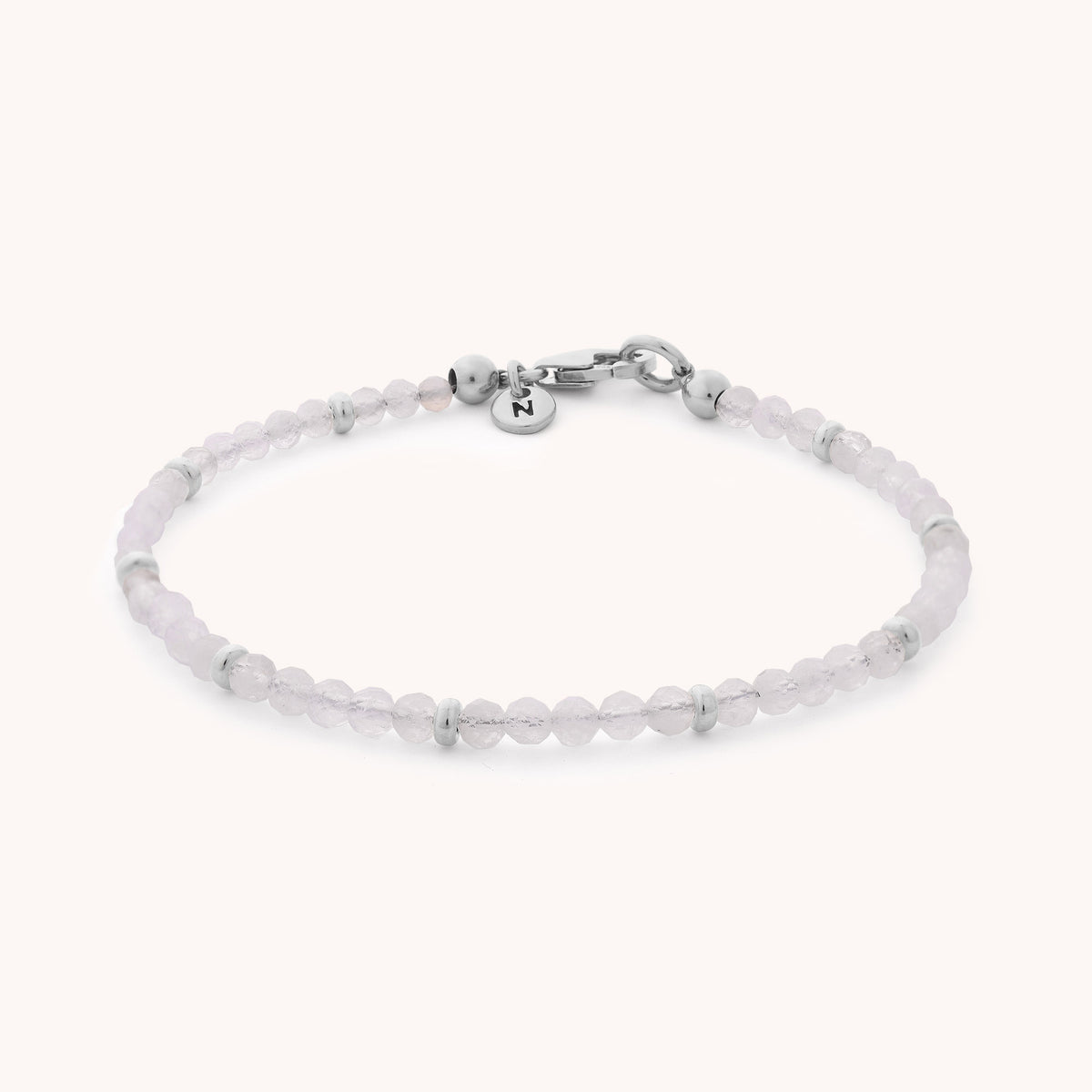 Delicate and handcrafted, the Rainbow Moonstone Orbit Bracelet - June features small, round pale pink beads accented with silver spacers, a silver clasp, and a round charm engraved with the letter N. Elegant on its own or layered, it makes an ideal June birthstone gift.