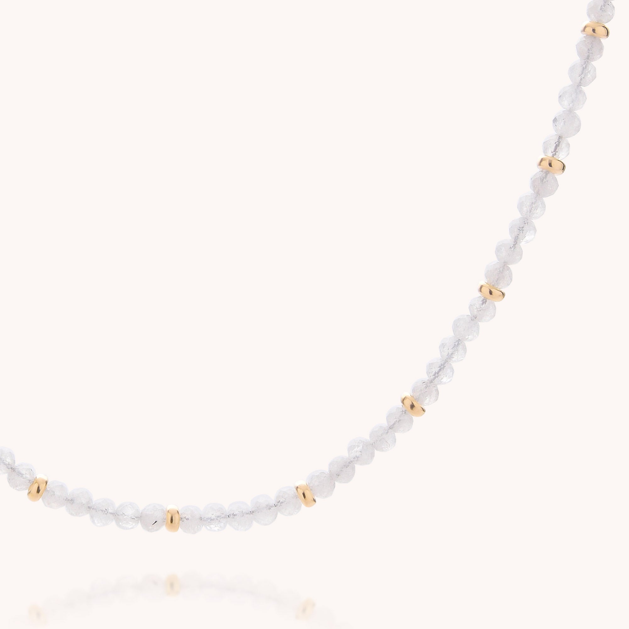 A close-up of the Rainbow Moonstone June Birthstone Orbit Necklace showcases small, clear round beads accented by evenly spaced gold beads, all displayed against a plain light background—highlighting the necklace’s delicate beauty and making it an ideal accessory for those celebrating a June birthday.