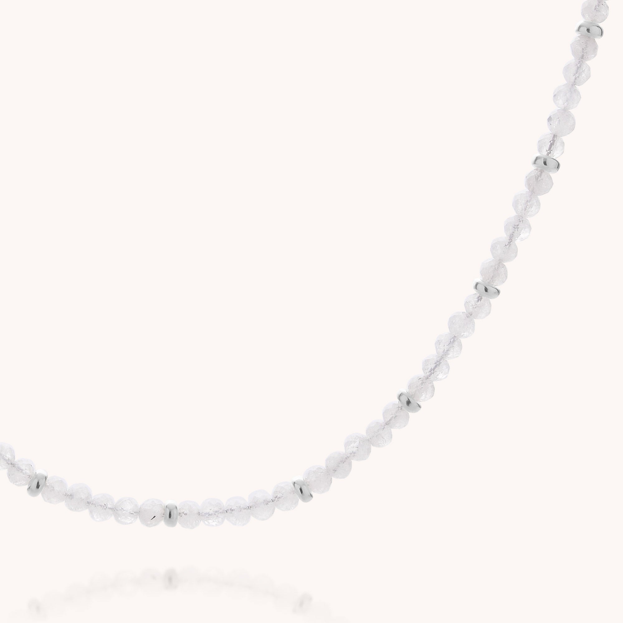 A close-up of the Rainbow Moonstone June Birthstone Orbit Necklace, showcasing its delicate design with small, round, translucent white beads reminiscent of rainbow moonstone and accented by shiny silver spacer beads, set against a light background.