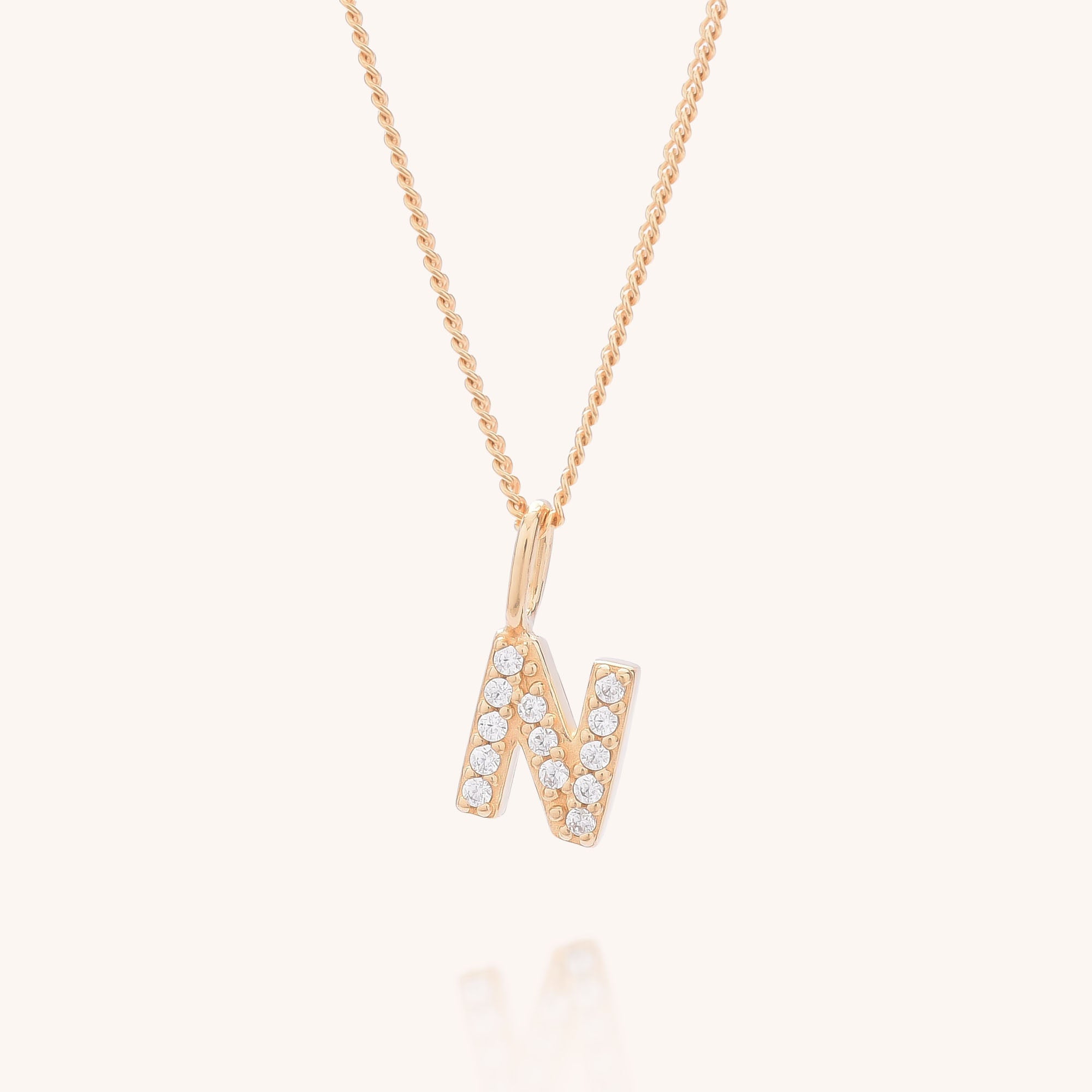 The Initial Sparkle Necklace features a gold chain with an N-shaped pendant adorned with sparkling cubic zirconia, creating a stunning personalized necklace.