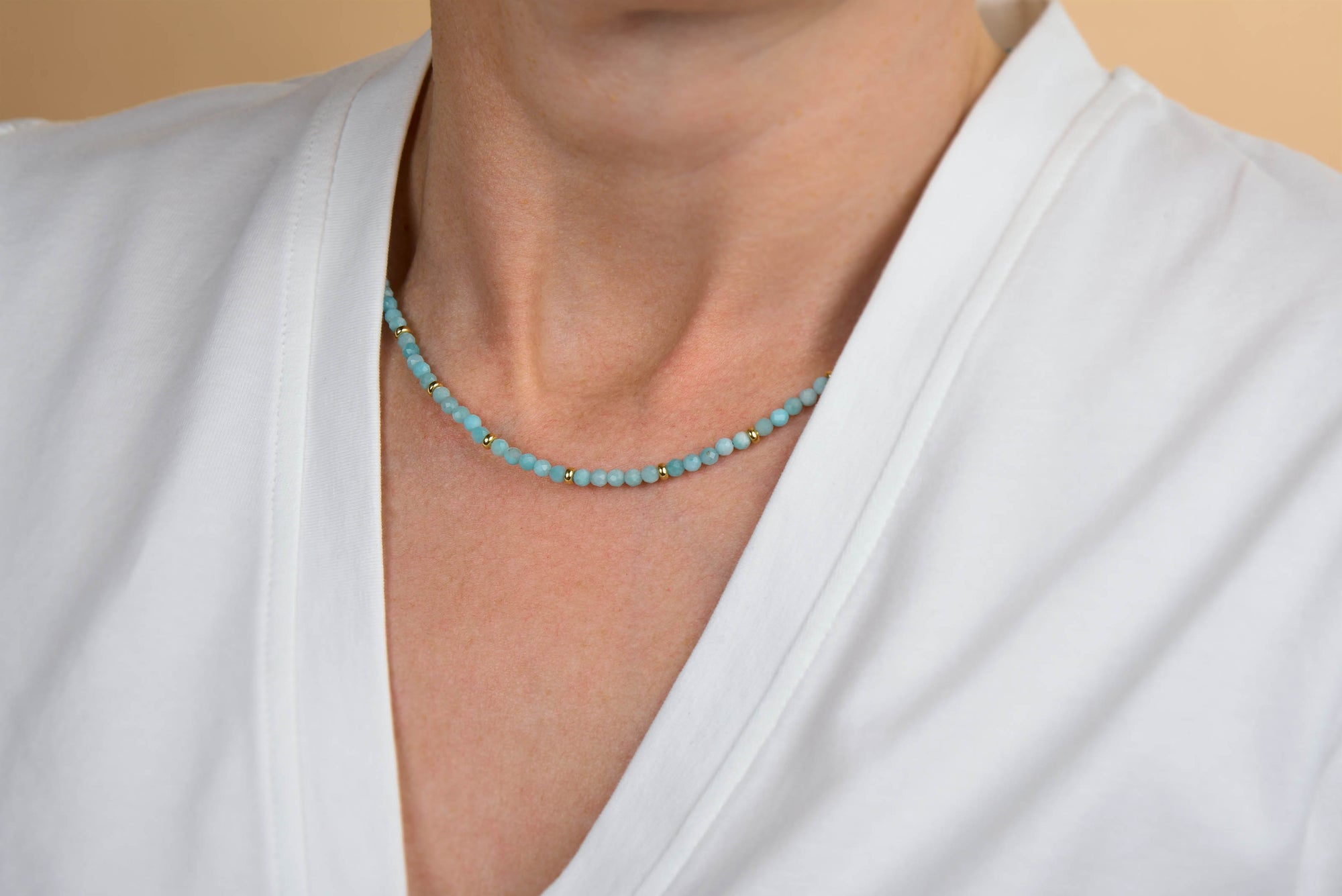 A person wearing a white V-neck shirt and the Amazonite Orbit Necklace, a delicate handcrafted piece featuring natural amazonite gemstones, around their neck.