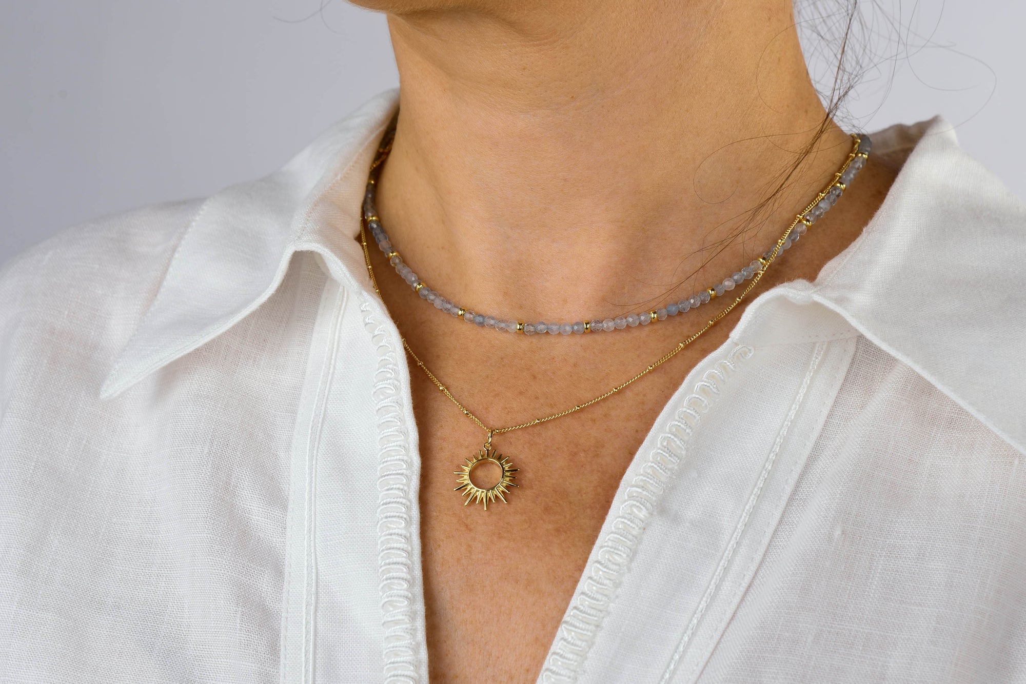 A person wearing a white shirt has two necklaces: a beaded choker and the Sol Necklace, which features a gold-plated sterling silver sun-shaped pendant.