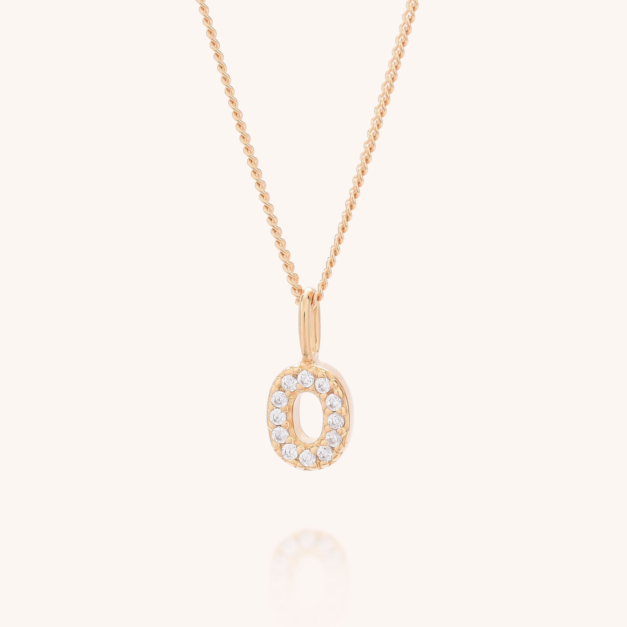 The Initial Sparkle Necklace is a gold pendant shaped like the letter O, accented with sparkling cubic zirconia, offering personalized elegance displayed against a light background.