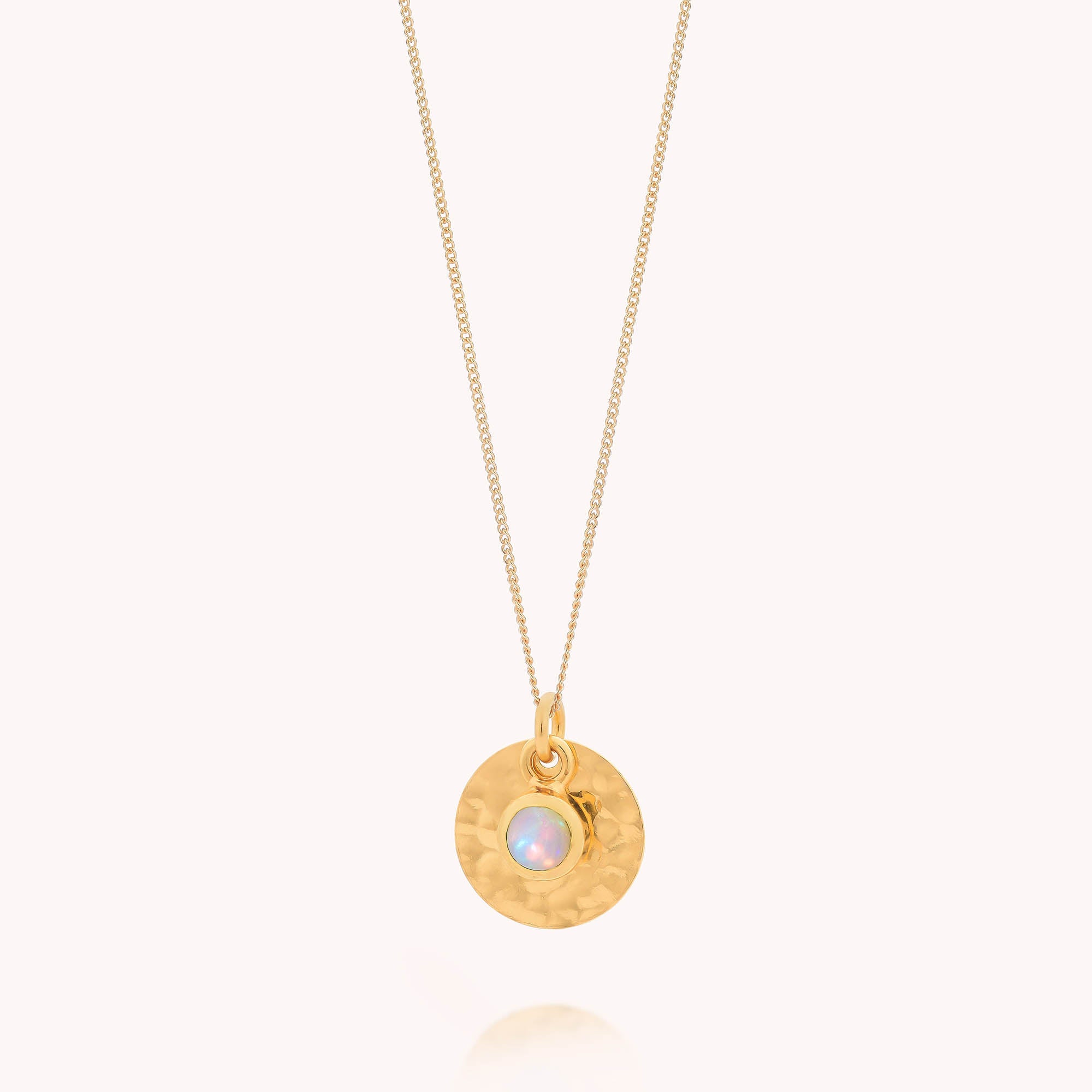 The Ethiopian Opal Luna Disc Necklace showcases a thin gold chain with a hammered disc pendant and a small Ethiopian opal, the October birthstone, both set in gold and hanging together.