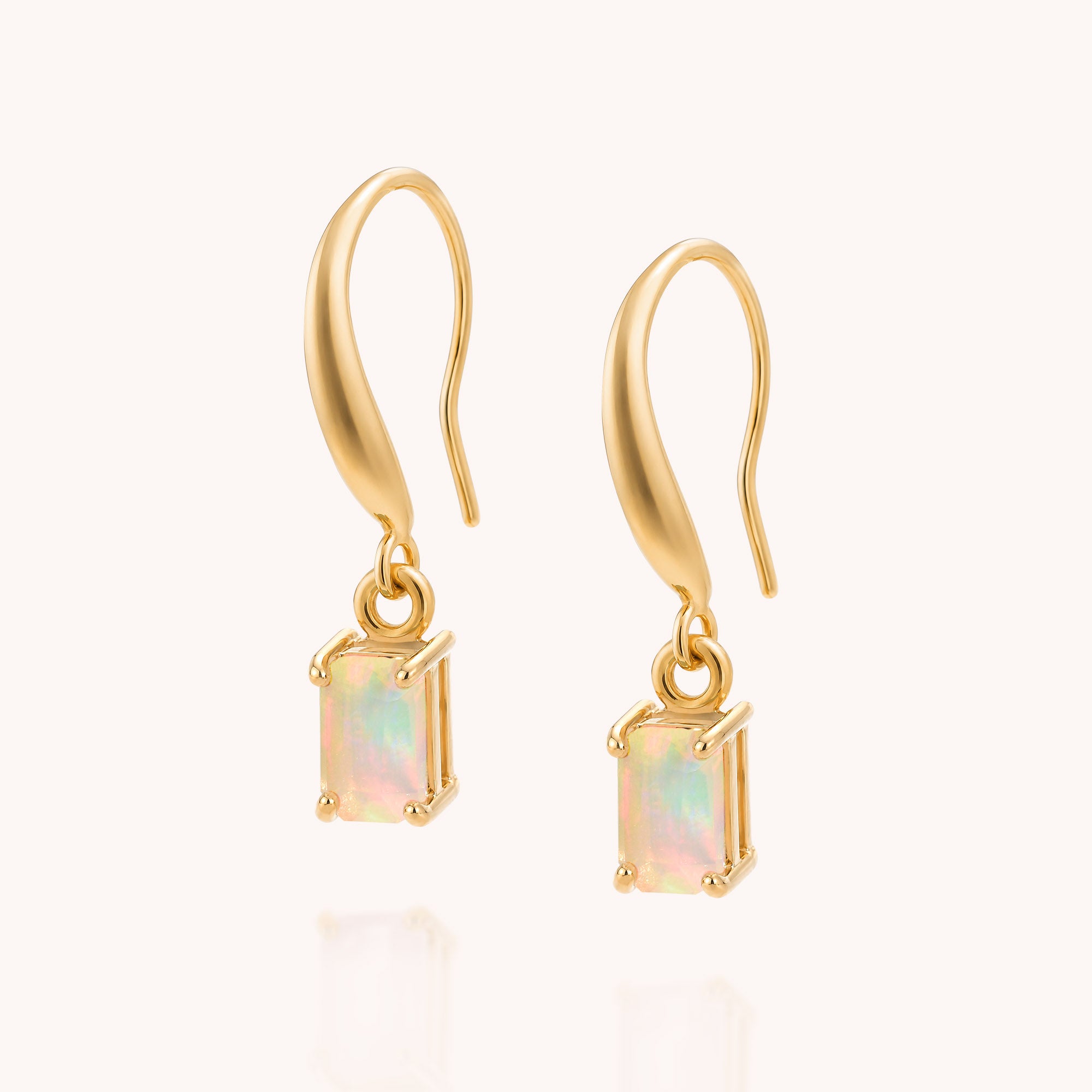 The Opal Octavia Drop Earrings feature rectangular Ethiopian opal gemstones in prong settings on curved gold hooks, elegantly displayed on a cream background.