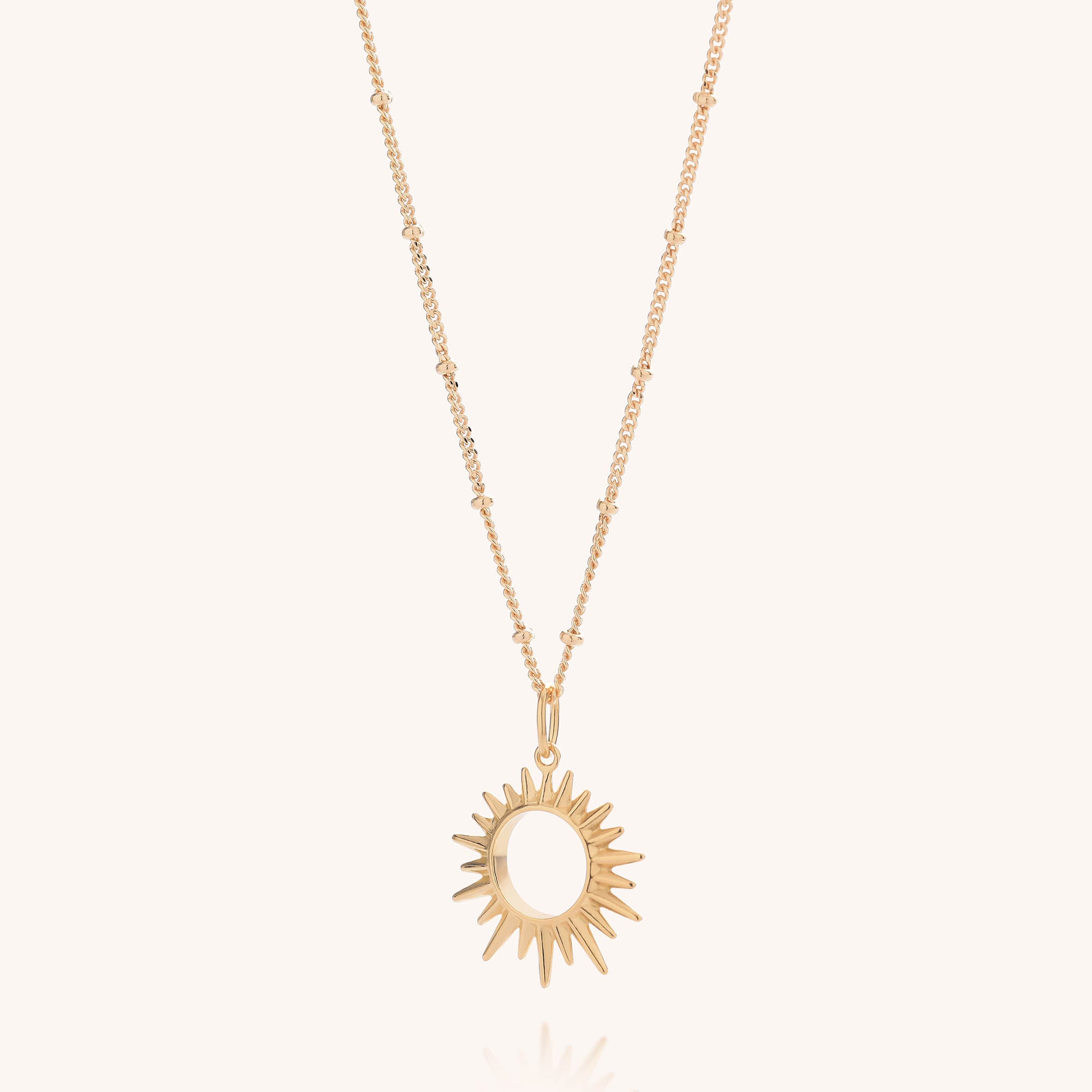 The Sol Necklace features a gold-plated sterling silver chain, delicately adorned with small beads and an eye-catching sun-shaped pendant with pointed rays, displayed against a plain, light background.