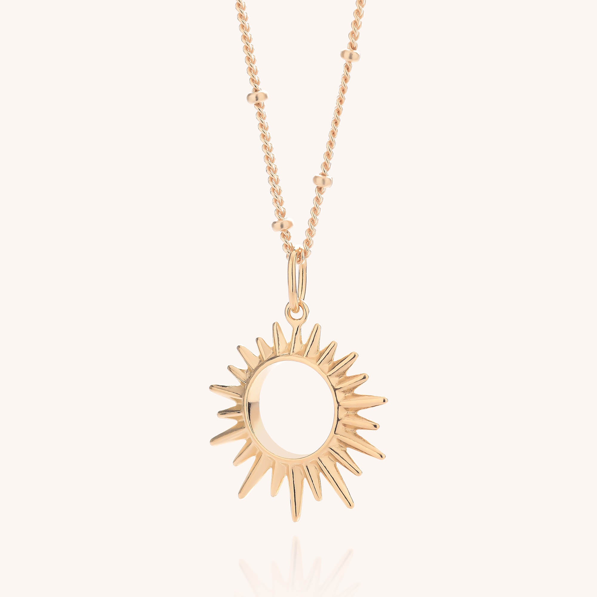 Introducing the Sol Necklace: a stunning gold-plated sterling silver piece featuring a sunburst-shaped pendant with a circular cutout center. The delicate chain is adorned with small bead accents and offers an adjustable length for the perfect fit, beautifully displayed against a light background.