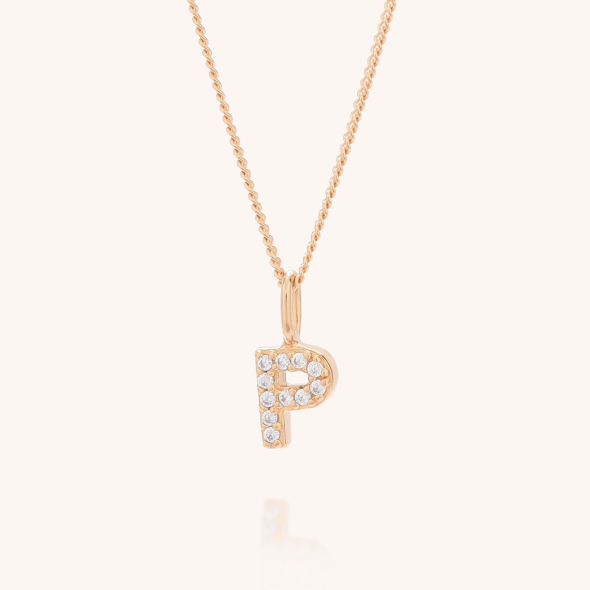The Initial Sparkle Necklace features a gold pendant in the shape of the letter P, adorned with sparkling cubic zirconia stones, and is showcased against a simple light background.