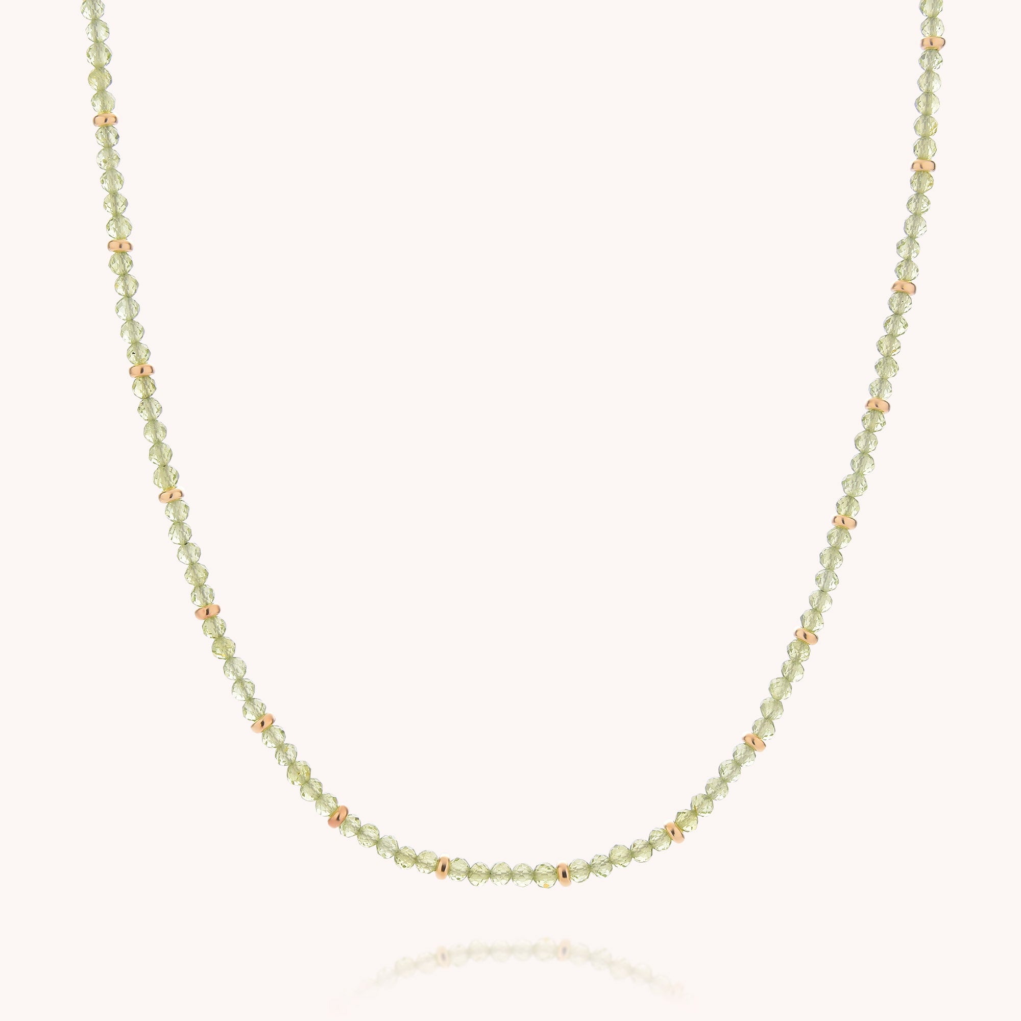 The Peridot August Birthstone Orbit Necklace showcases a refined strand of small, faceted light green peridot beads accented with tiny gold beads throughout, creating a simple yet elegant design against a plain light background—an understated homage to the August birthstone.