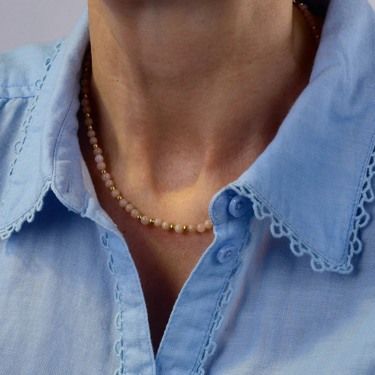 A person wearing a light blue collared shirt with lace trim and the Pink Opal October Birthstone Orbit Necklace around their neck.
