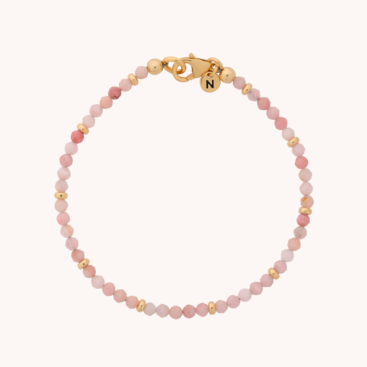The Pink Opal Orbit Bracelet – October features delicate, handcrafted small round pink opal beads and gold accents, finished with a gold clasp and a petite round charm engraved with the letter N—an elegant tribute to the October birthstone.