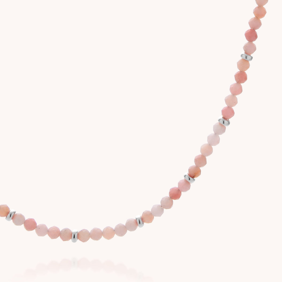 A close-up of the Pink Opal October Birthstone Orbit Necklace, showcasing its handcrafted design with alternating small pink, peach, and silver beads against a plain light background.