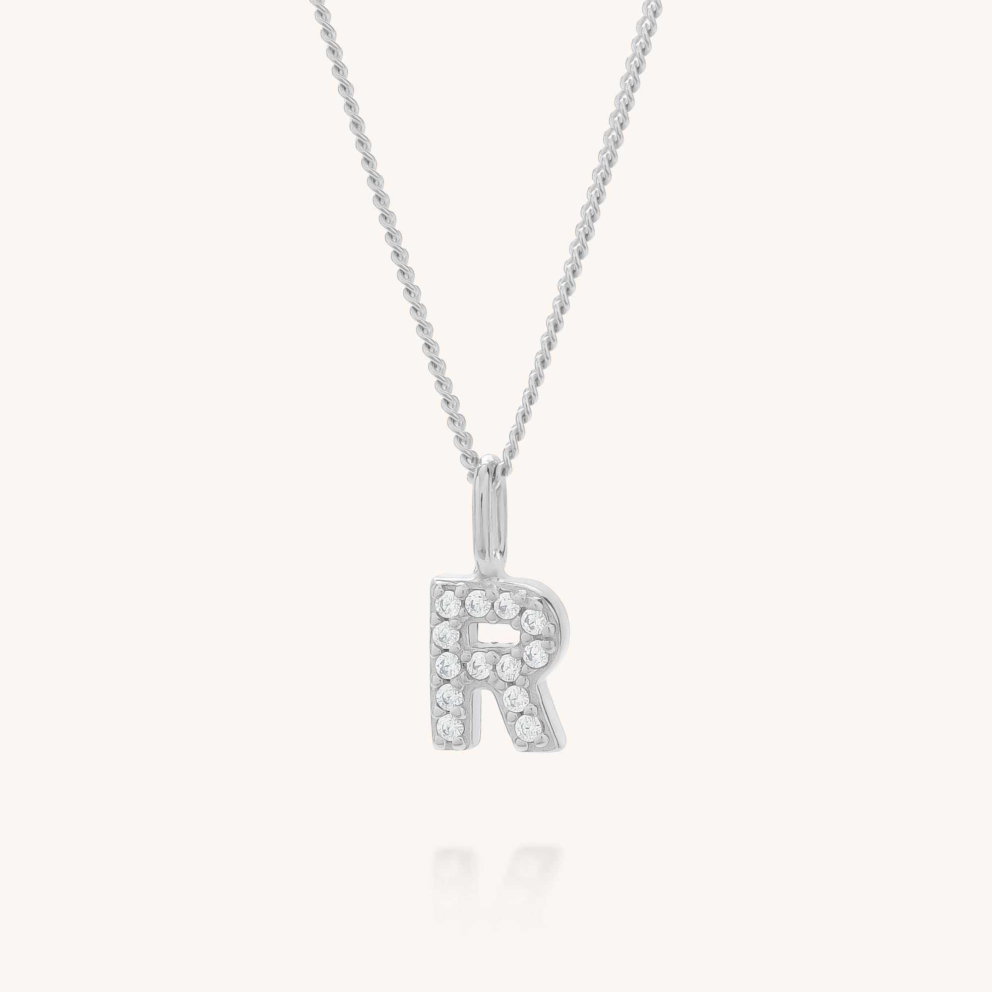 The Initial Sparkle Necklace showcases a silver letter R pendant adorned with glimmering cubic zirconia, set against a plain white background.