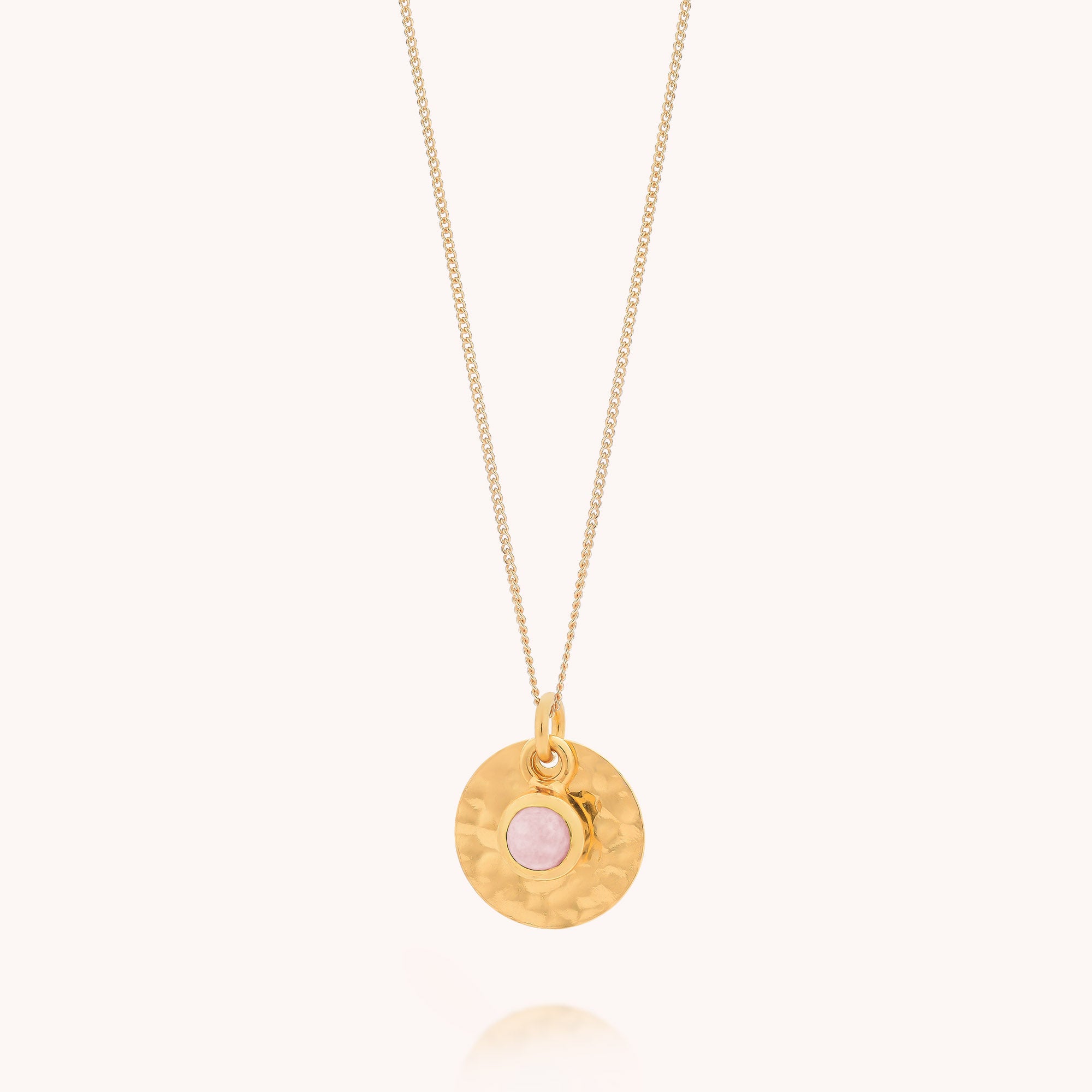 Introducing the Rose Quartz Luna Disc Necklace: a gold plated sterling silver piece featuring a fine chain and a round hammered disc pendant, accented by a delicate rose quartz stone set at its center. Displayed against a plain, light-colored background, this necklace’s elegant design is beautifully highlighted.