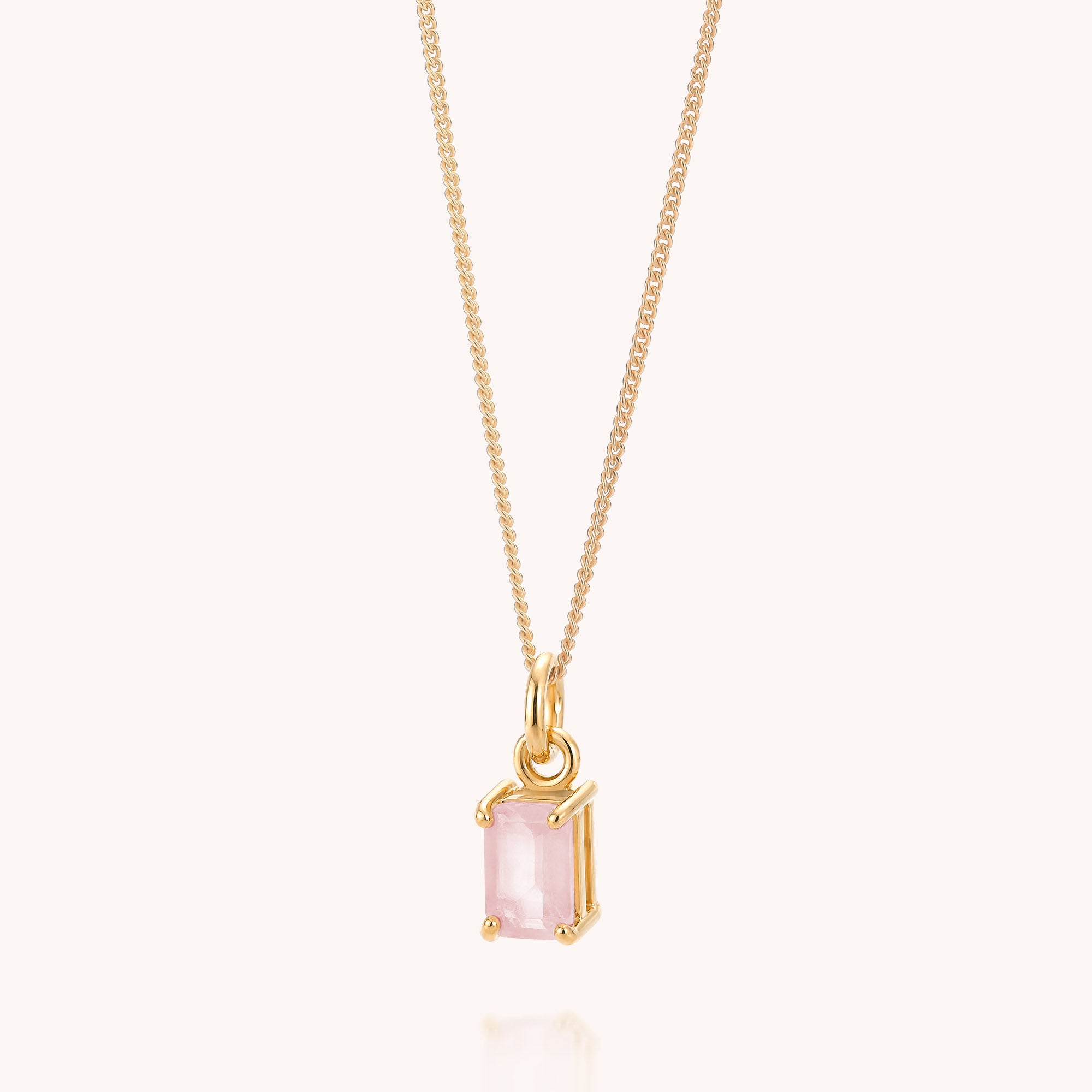 The Rose Quartz Octavia Necklace, featuring a rectangular pink gemstone pendant, hangs against a plain, light background.