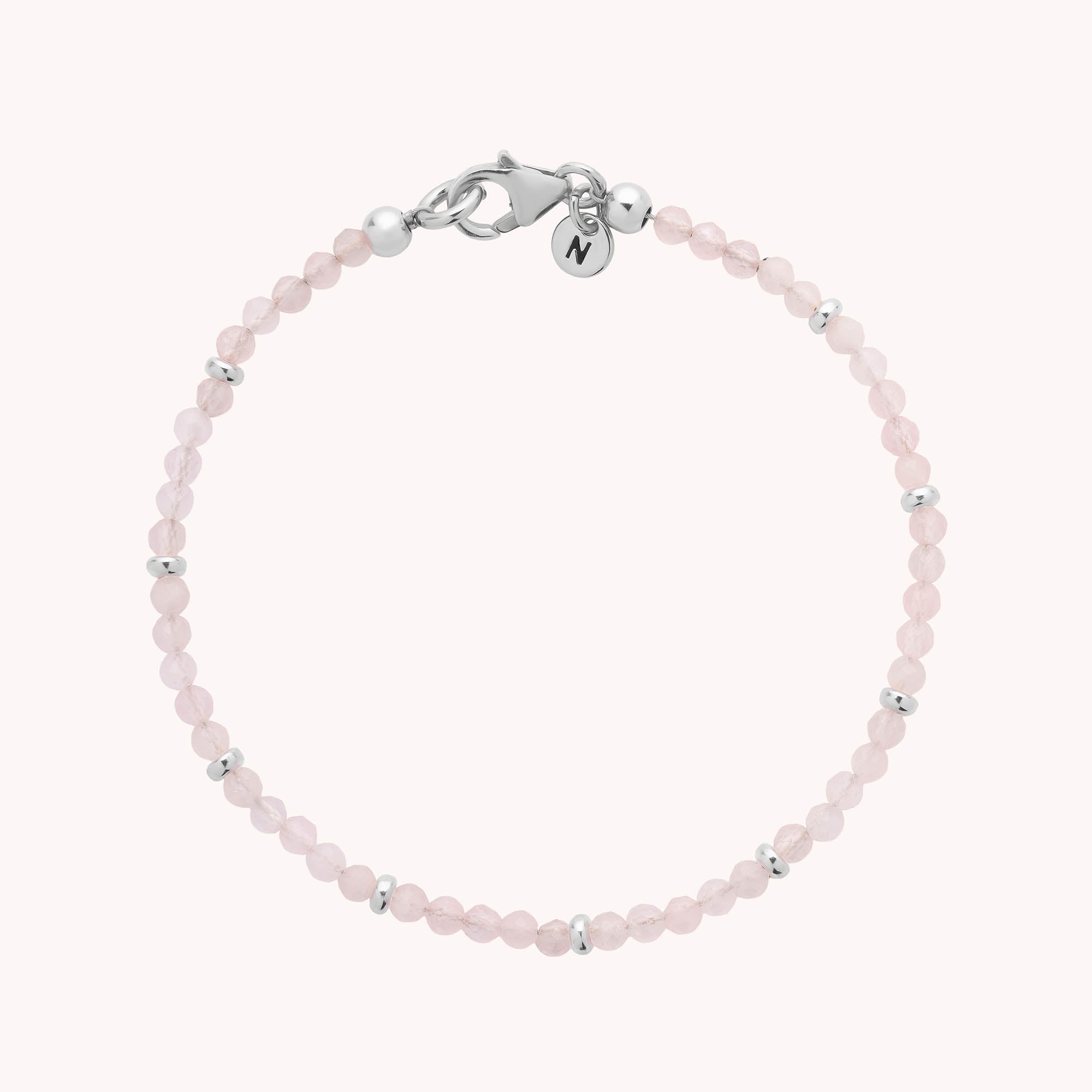 Introducing the Rose Quartz Orbit Bracelet: a delicate design crafted with faceted rose quartz beads and small sterling silver spacers, finished with a silver lobster clasp and a round charm engraved with the letter M.