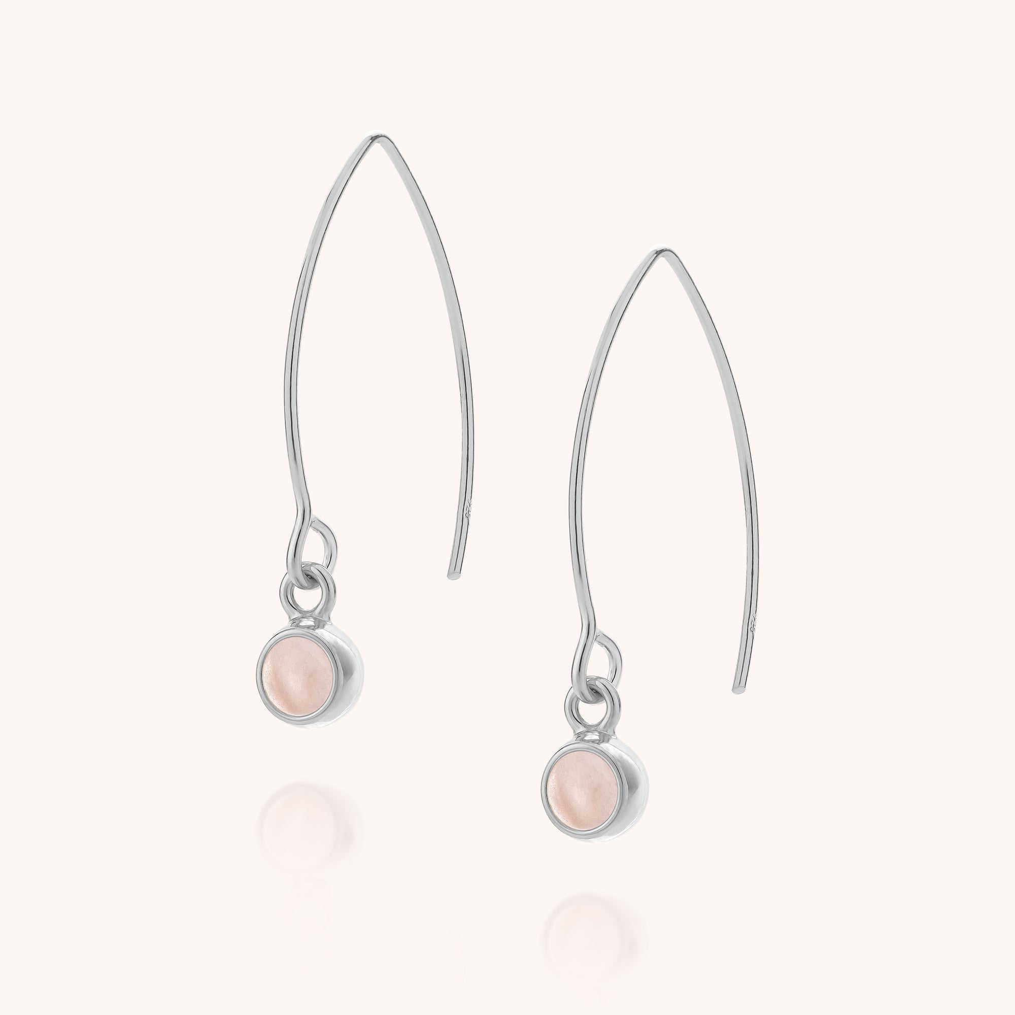 Introducing the Rose Quartz Gem Dot Arc Earrings: a pair of silver arc earrings with elongated hooks, each adorned with a small, round, pale pink rose quartz gemstone set in a bezel setting at the bottom.