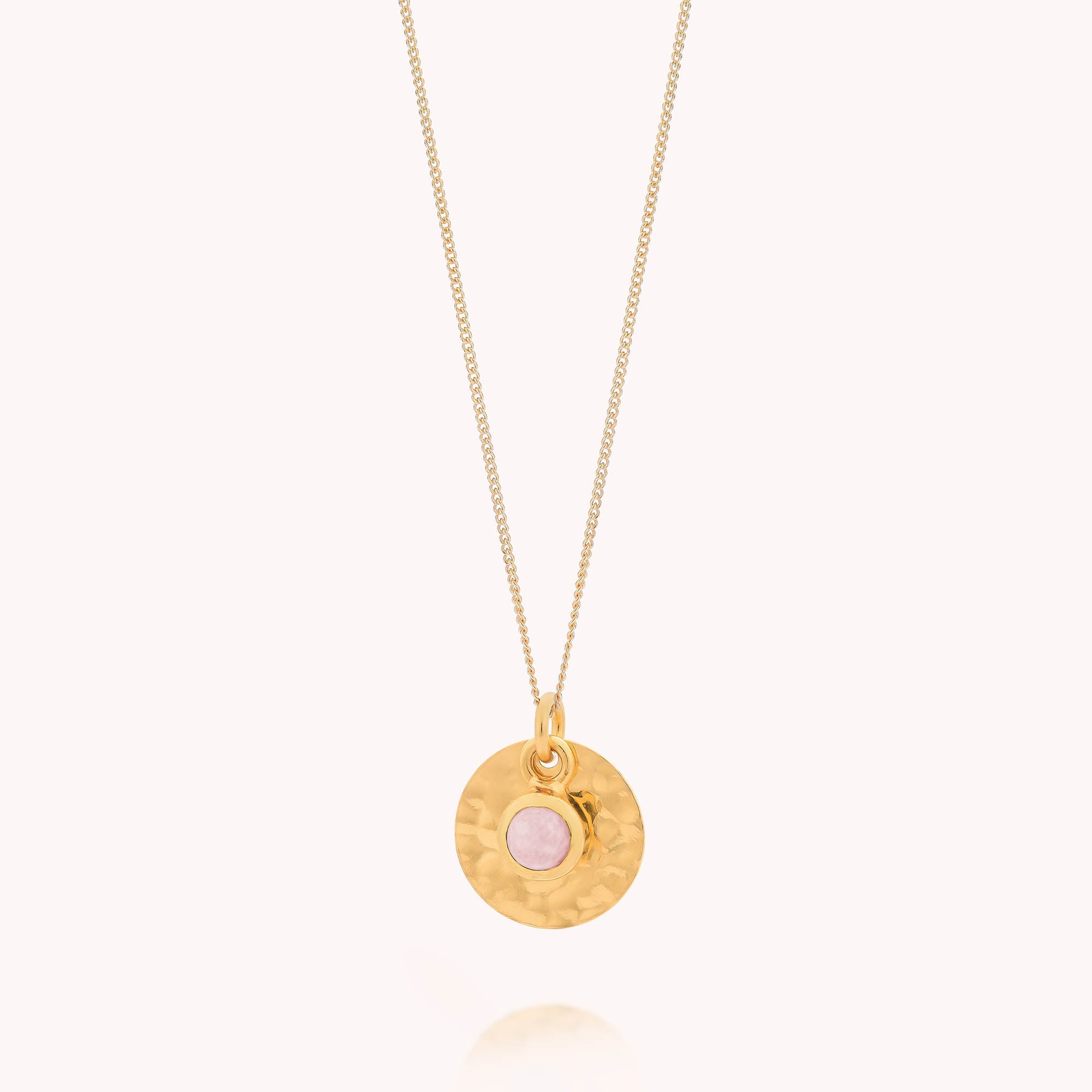 Gold necklace with a round pendant featuring a pink stone on a white background