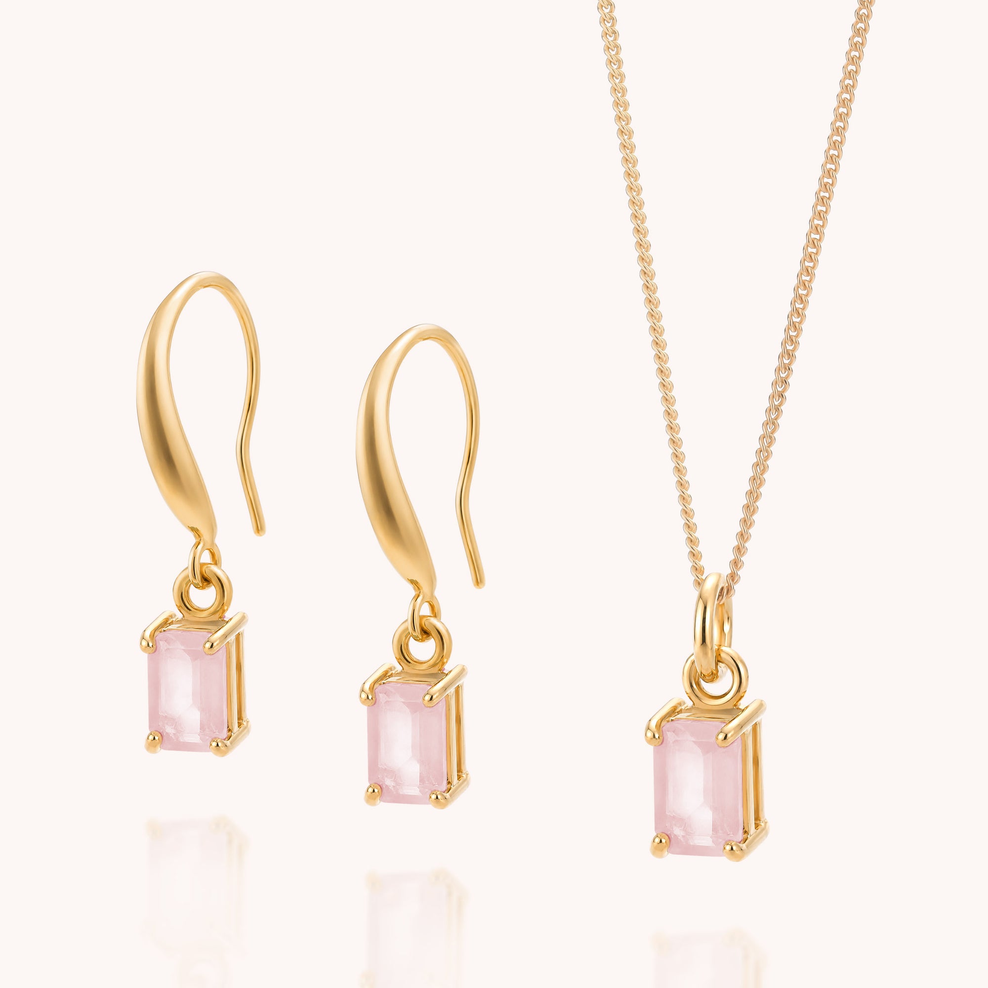 The Rose Quartz Octavia Necklace & Earrings Set features gold jewelry adorned with pale pink rectangular rose quartz gemstones, including a pair of hook earrings and a matching pendant necklace, displayed on a light background.