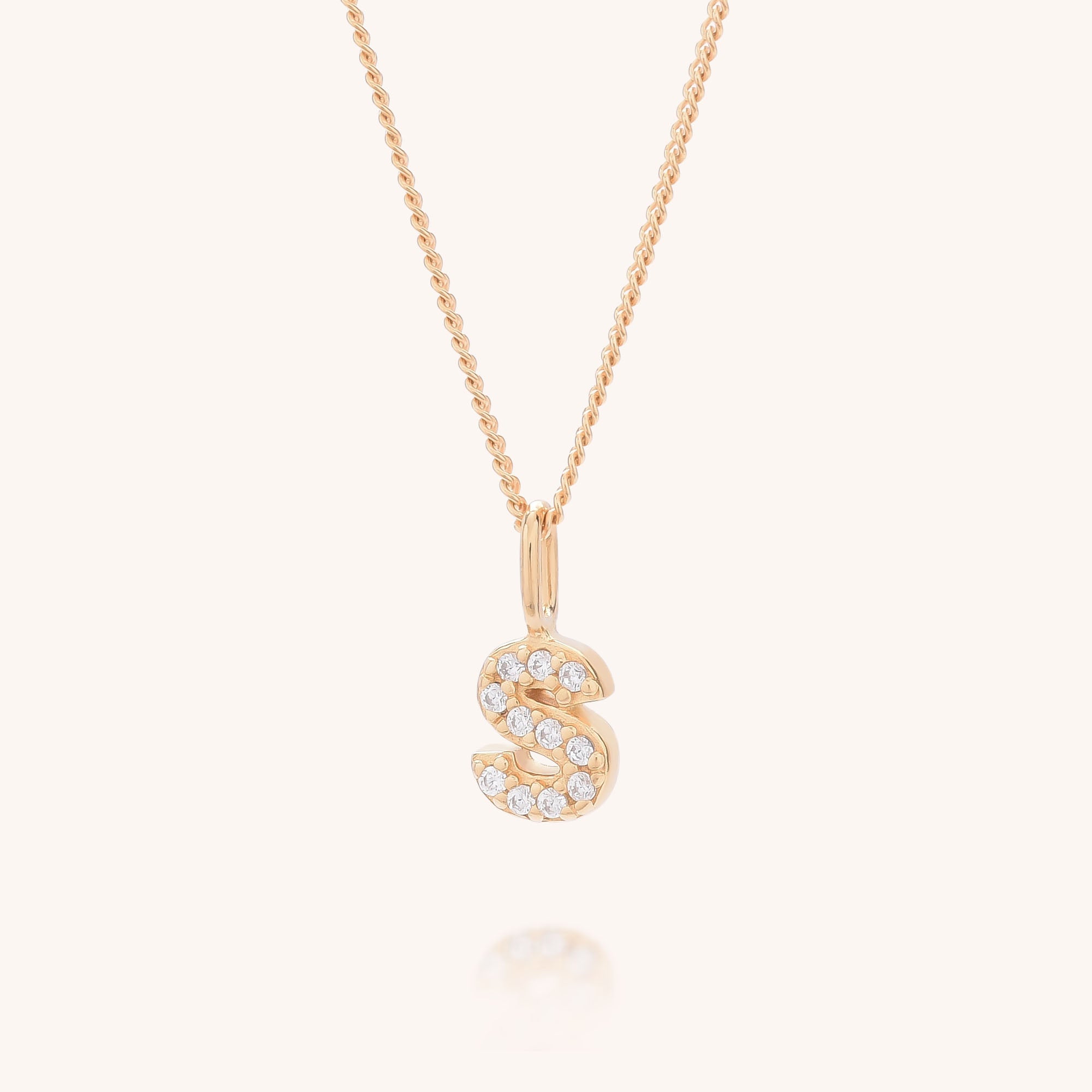 The Initial Sparkle Necklace is a gold necklace with an &quot;S&quot;-shaped pendant adorned with sparkling cubic zirconia, shown against a plain, light background.