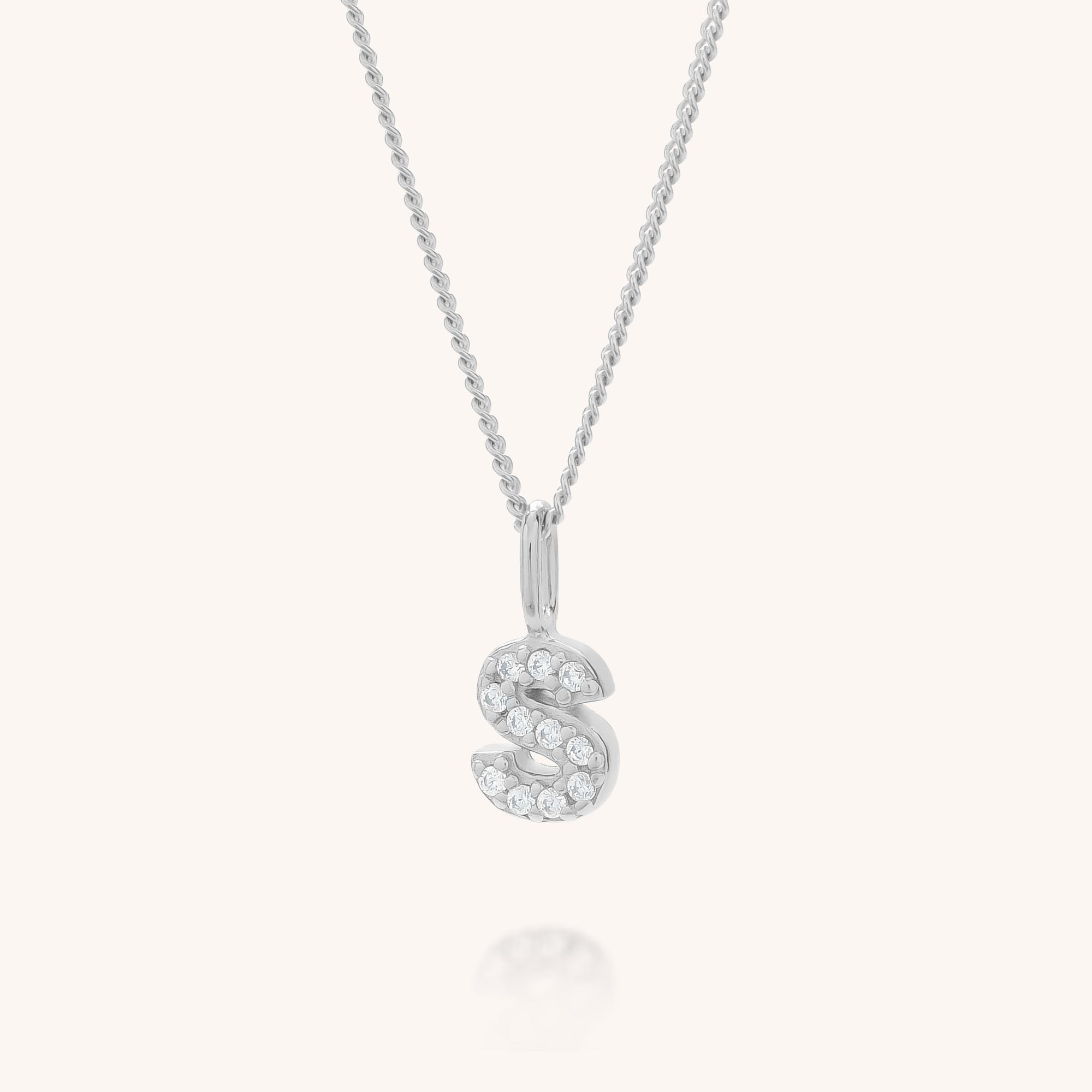 The Initial Sparkle Necklace features a silver S-shaped pendant embellished with sparkling cubic zirconia, displayed on a simple light background.