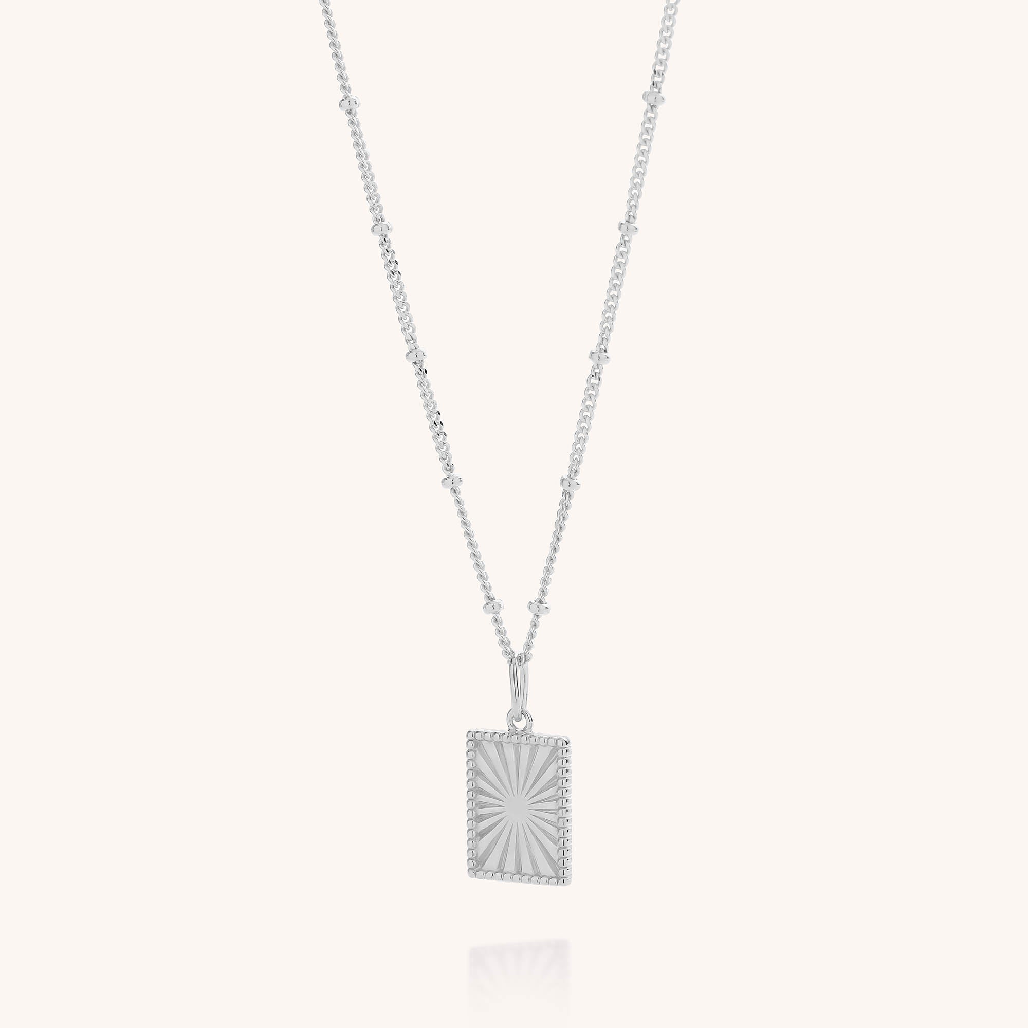 Sunray Necklace featuring a beaded chain and a rectangular pendant etched with a striking sunburst pattern, photographed on a plain white background.