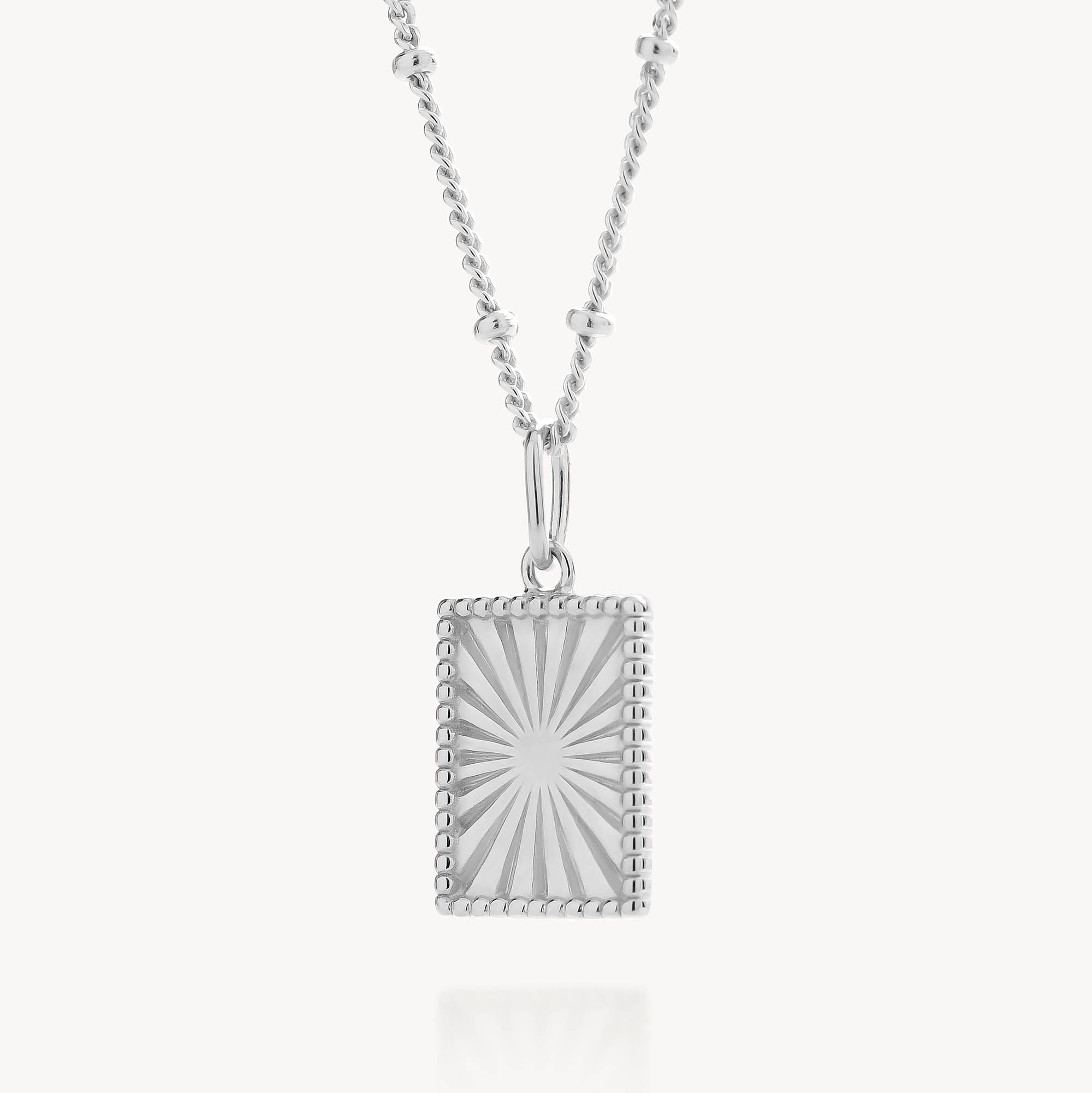 The Sunray Necklace showcases a rectangular sterling silver pendant with a bold sunburst design and beaded edges, gracefully hanging from a delicate chain accented with small round details.