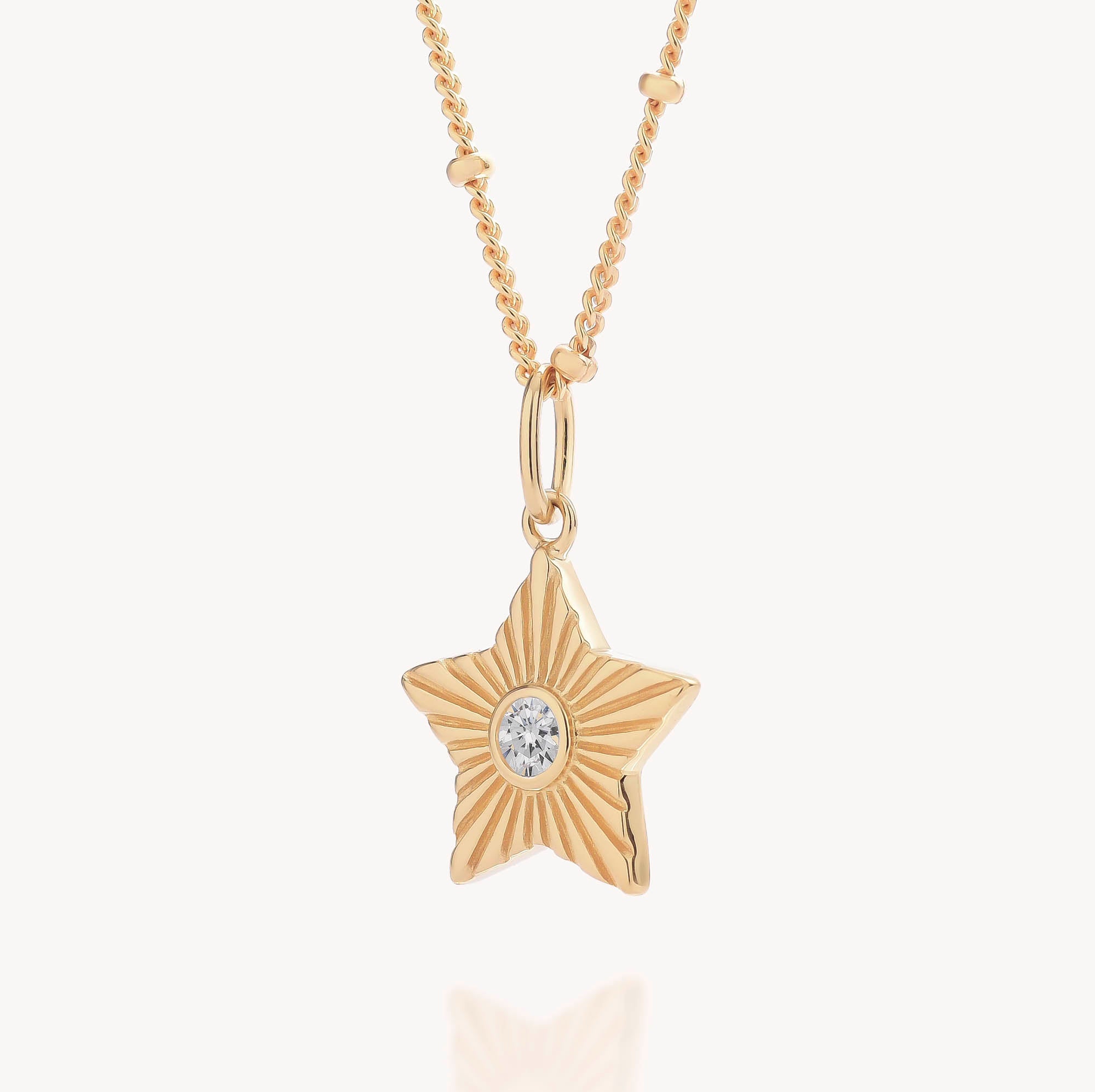 Astrid Star Necklace: A gold star-shaped pendant necklace featuring a central cubic zirconia gemstone and a textured, radiating pattern. The chain is embellished with small decorative beads, shown against a plain white background.