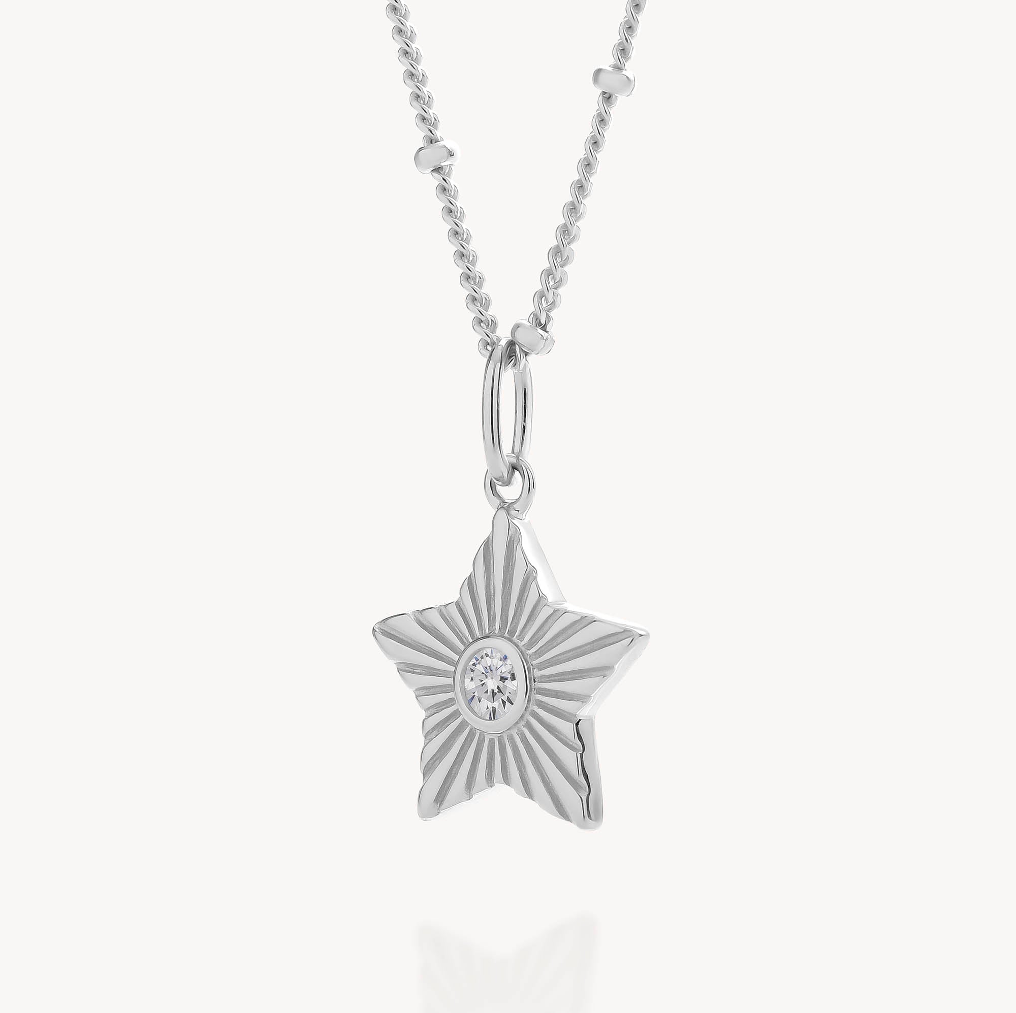 The Astrid Star Necklace features a silver, star-shaped pendant with a textured design and a sparkling clear cubic zirconia gemstone at the center. Displayed on a delicate chain against a white background, this dazzling necklace is the perfect statement piece for any occasion.