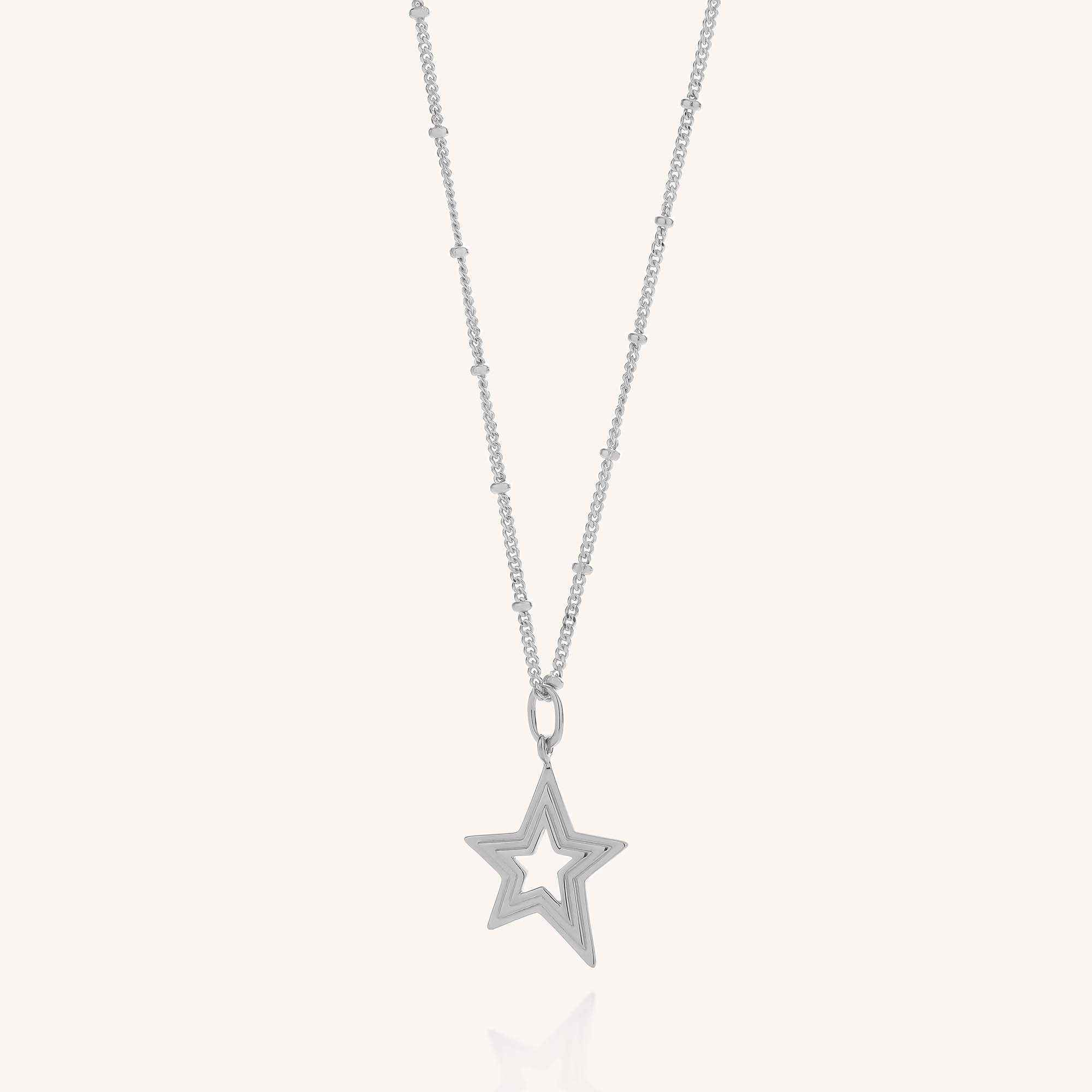 The Stellar Starburst Necklace features a delicate sterling silver chain adorned with small beads and a layered star pendant with a hollow center, elegantly showcased against a light background.