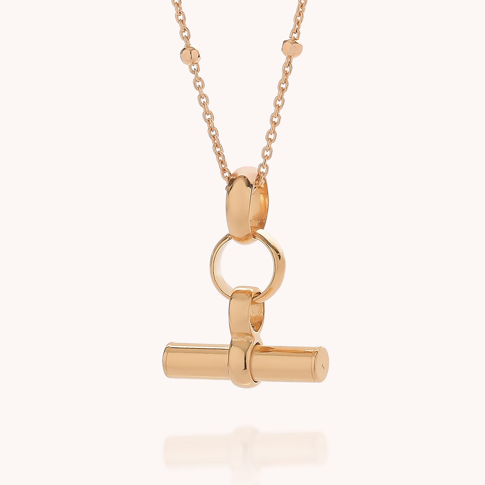 Mini T Bar Necklace showcasing a polished T-bar pendant with rounded edges and a circular link, displayed against a light background. This elegant piece features a refined satellite chain, giving the classic style of the Mini T Bar Necklace a modern update.