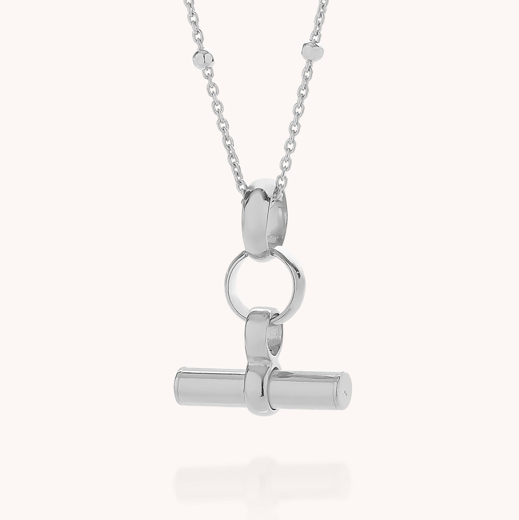 Introducing the Mini T Bar Necklace: a sterling silver pendant necklace showcasing a horizontal cylindrical T-bar linked to a sleek round ring, all suspended from a delicate satellite chain adorned with subtle bead accents.