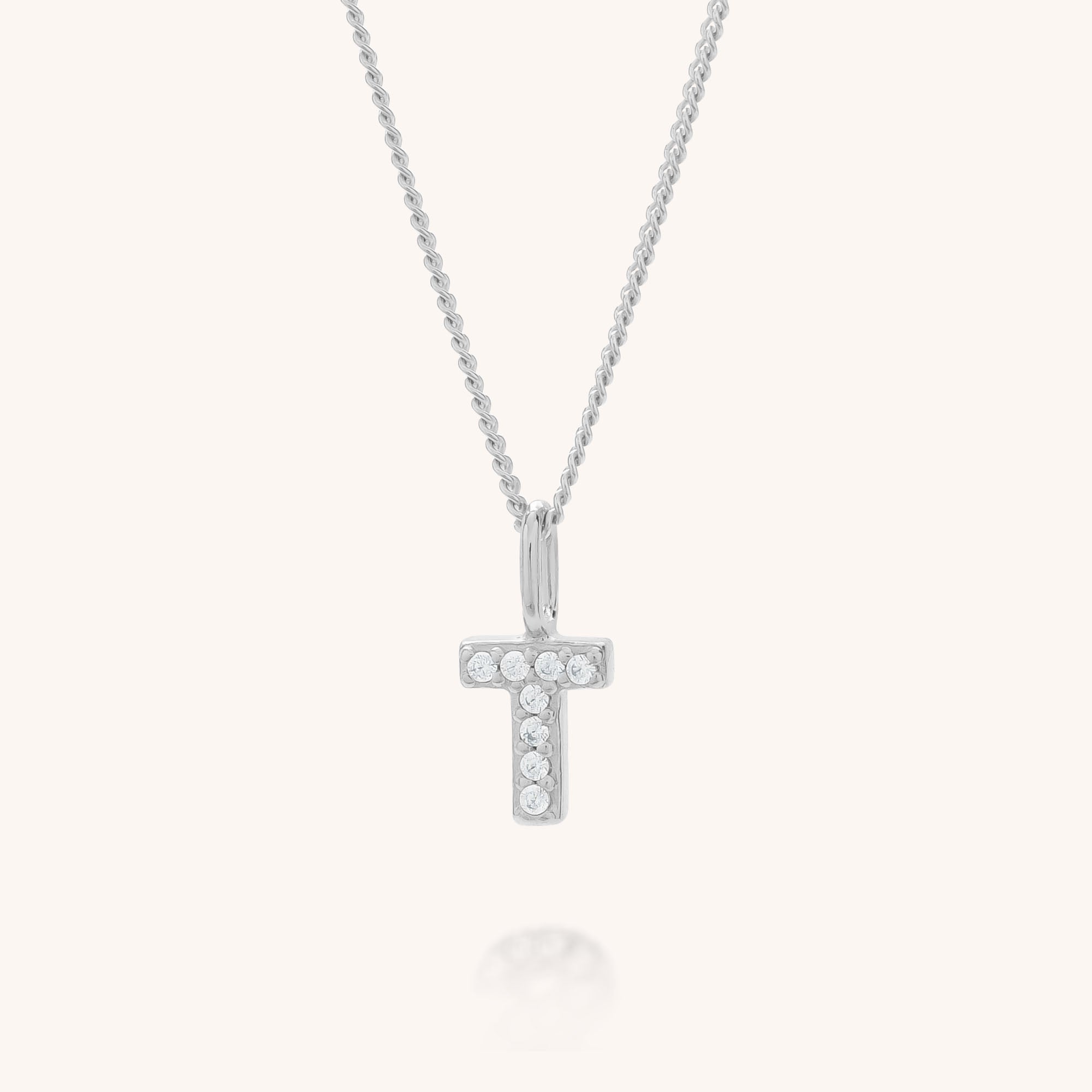 The Initial Sparkle Necklace showcases a silver pendant in the shape of the letter T, embellished with sparkling cubic zirconia stones and set against a simple, light background.