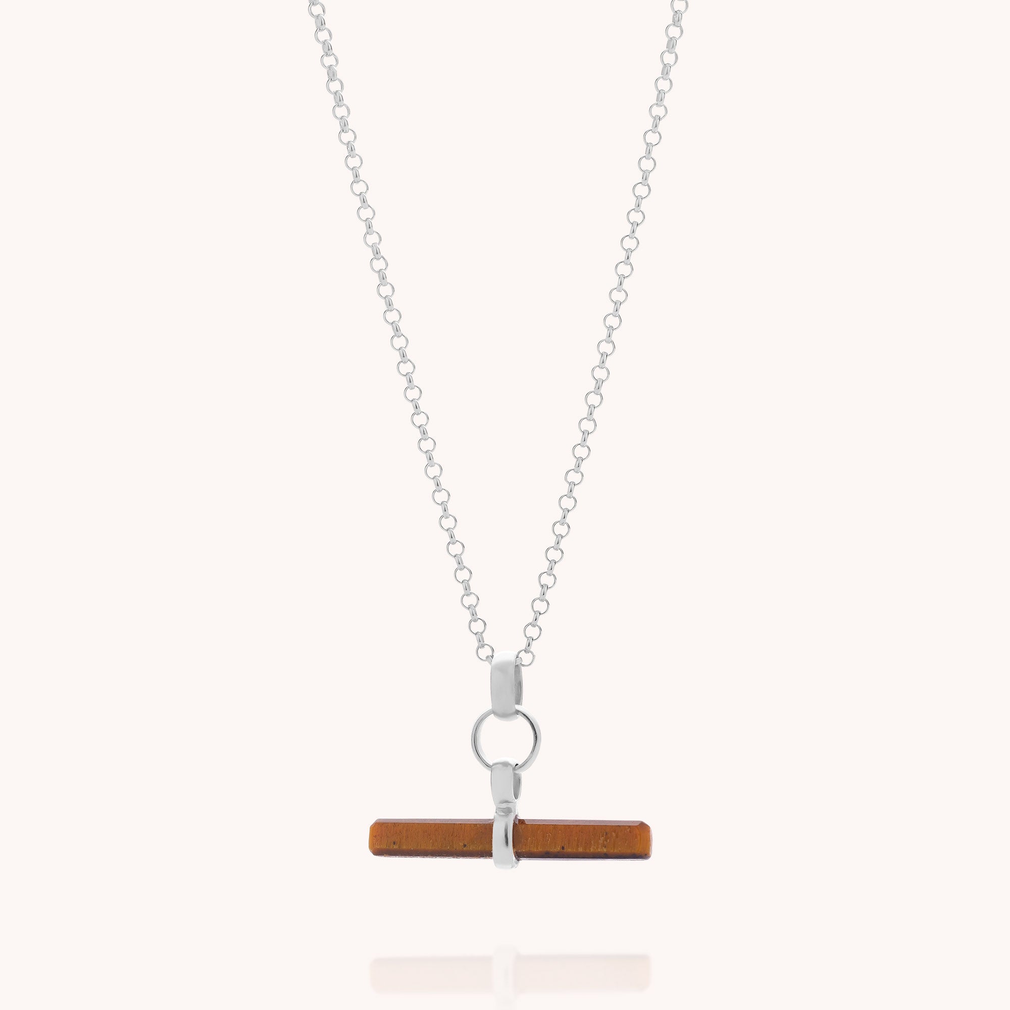 The Tiger Eye T-Bar Necklace features a silver chain with a horizontal rectangular tiger eye pendant, secured by a circular and two vertical metal loops. Displayed against a light background, this elegant necklace showcases the warm brown hues of the tiger eye gemstone.