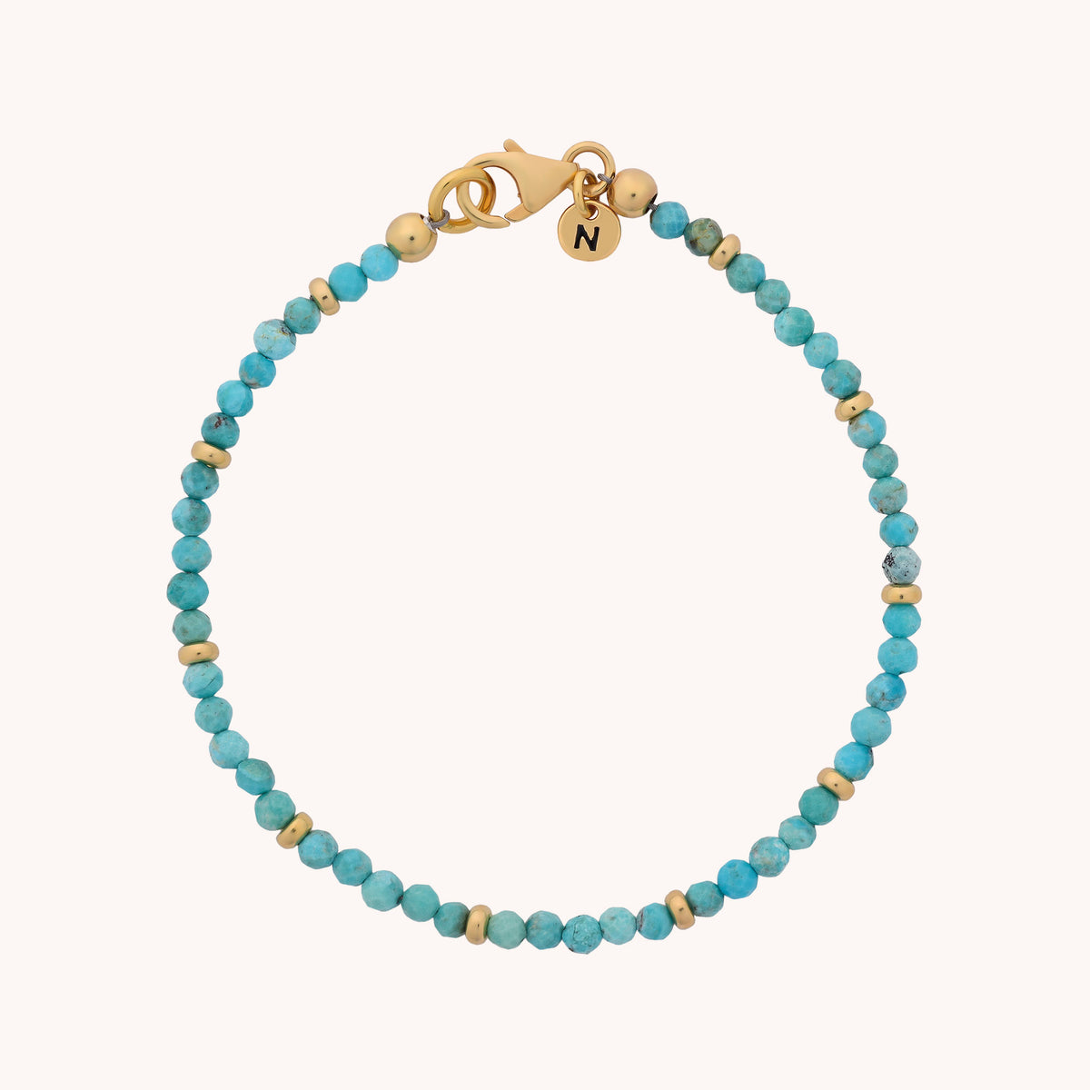 The Turquoise Orbit Bracelet - December is a delicate piece handcrafted with small turquoise beads and gold accents. It features a gold clasp and two elegant gold charms, one engraved with an “N”. Celebrating turquoise as the December birthstone, this bracelet adds both beauty and meaning to any jewelry collection.