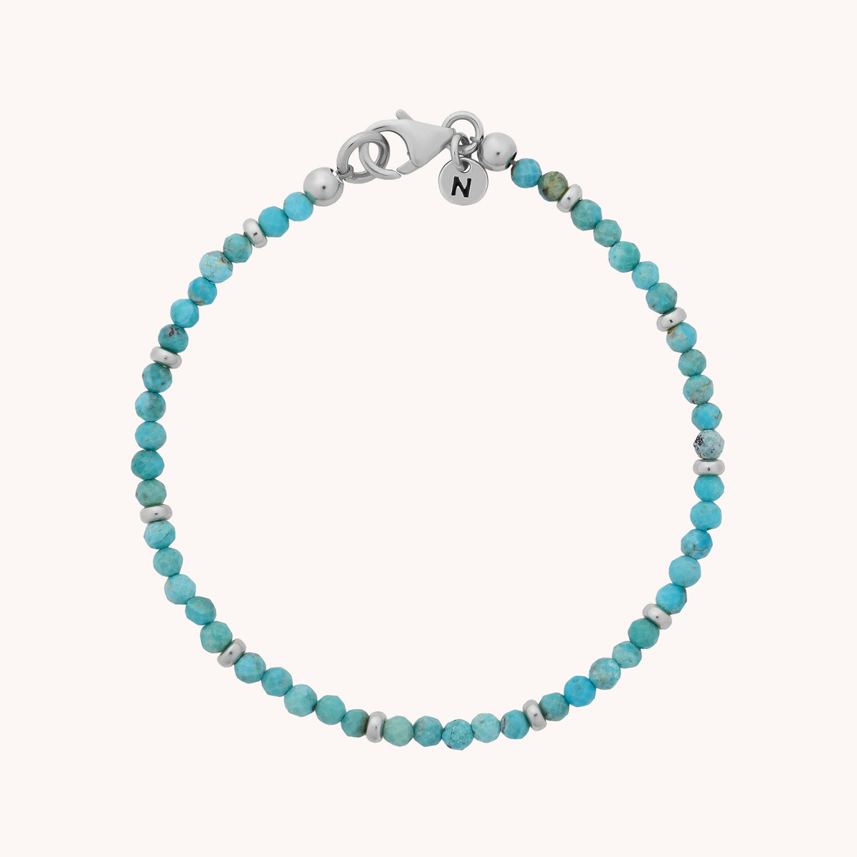 Introducing the Turquoise Orbit Bracelet - December: a handcrafted piece featuring small, marbled turquoise beads strung together and finished with a silver lobster clasp. Two delicate silver charms add unique detail, including one engraved with the letter N. Perfect for those who love distinctive jewelry, this bracelet makes a thoughtful gift—especially for anyone celebrating a December birthstone.