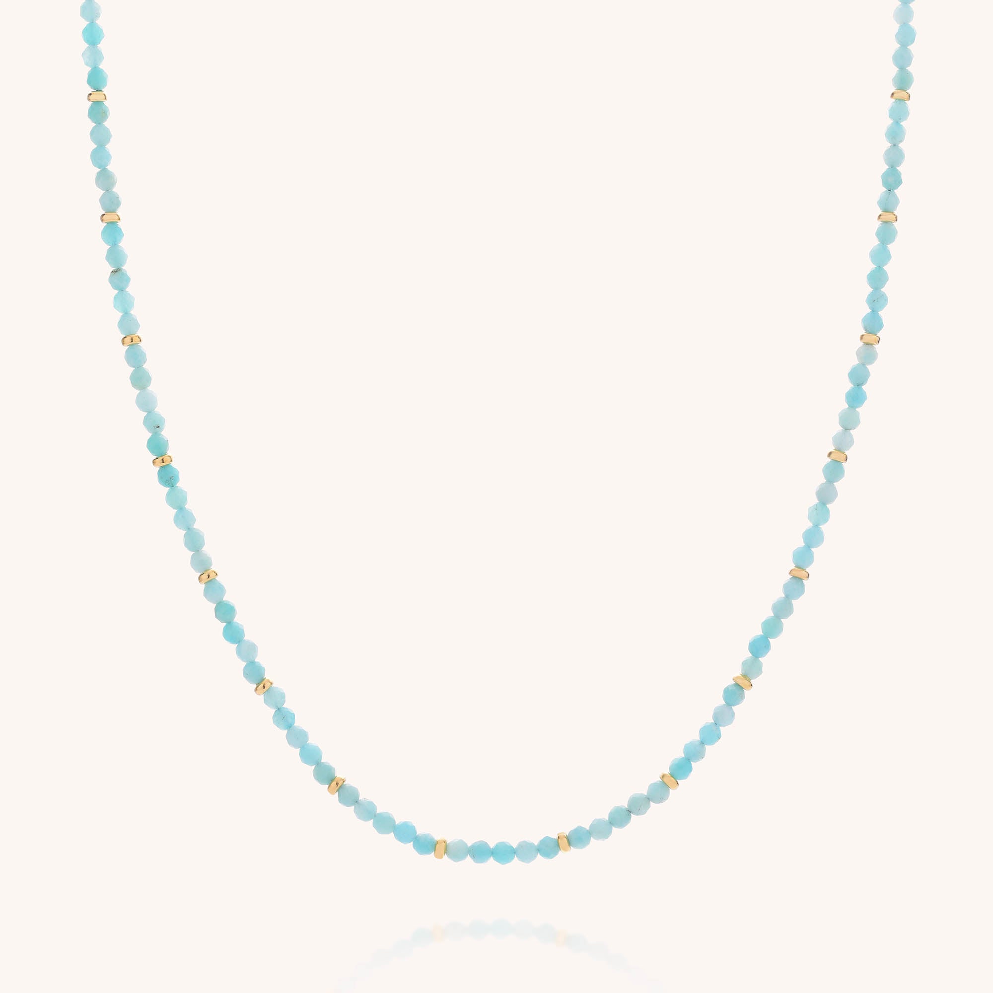 The Amazonite Orbit Necklace features small, round faceted amazonite beads in a soft light blue hue, each one evenly spaced with tiny gold-plated sterling silver accents and elegantly displayed against a plain white background.