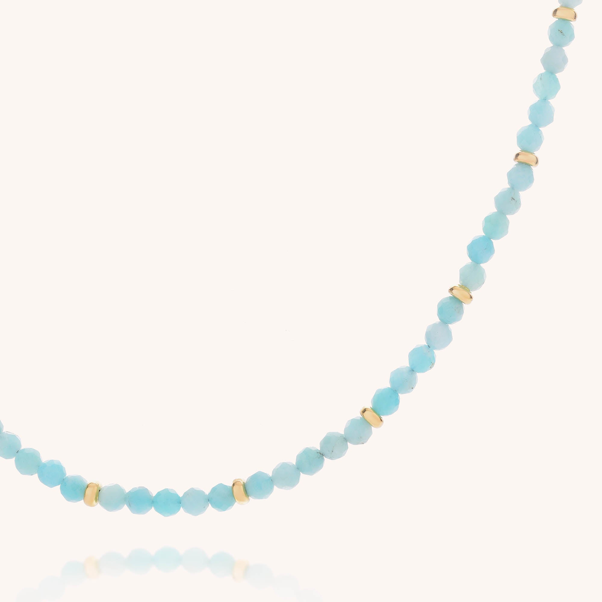 The Amazonite Orbit Necklace showcases small, round light blue faceted amazonite beads accented with gold plated sterling silver spacers, elegantly displayed on a white background.