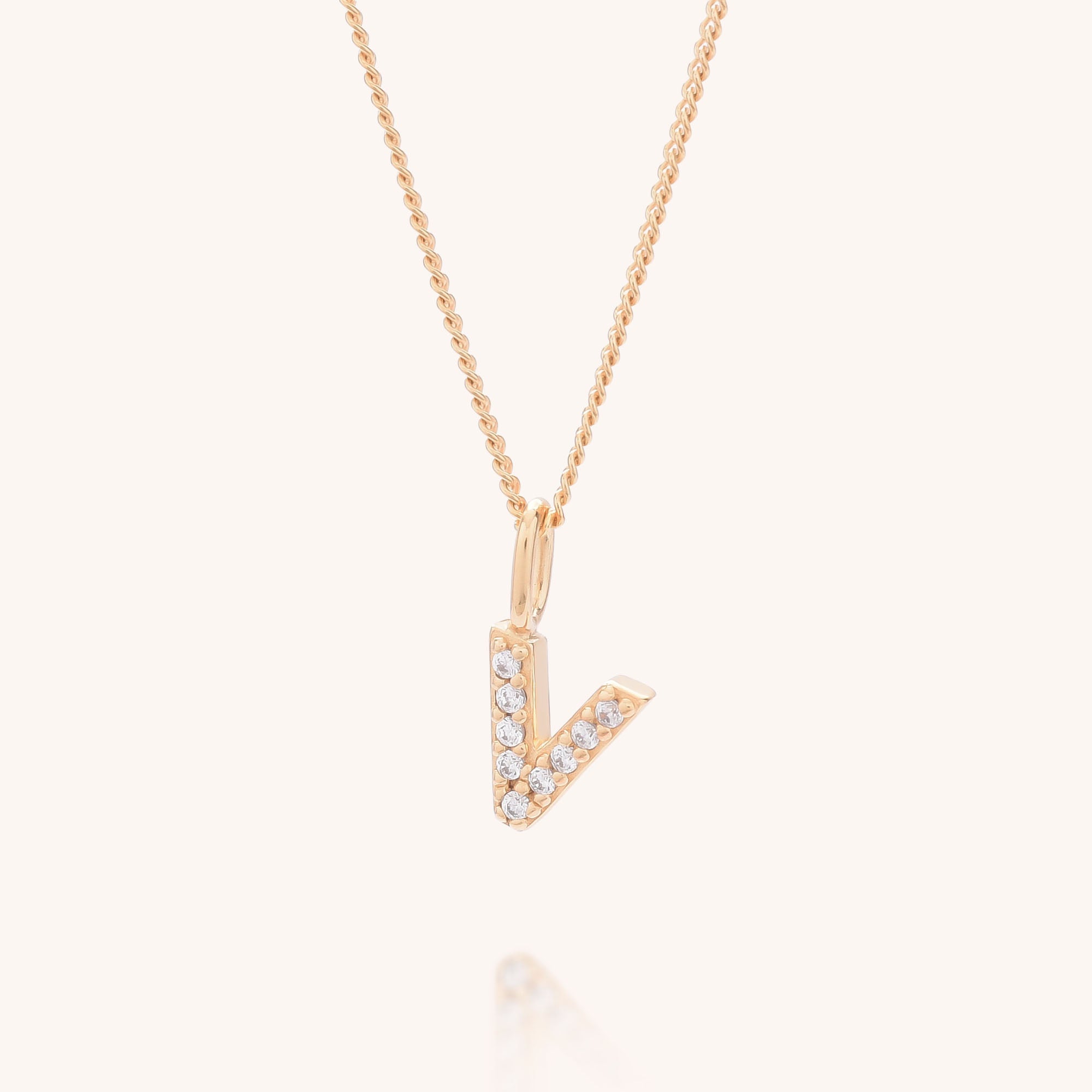 The Initial Sparkle Necklace is a gold chain with a V-shaped pendant adorned with sparkling cubic zirconia, shown against a plain light background in a modern, minimalist style.