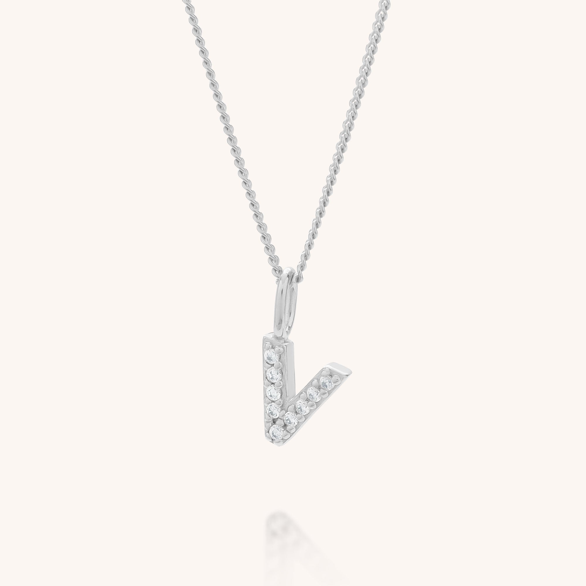 The Initial Sparkle Necklace features a delicate silver chain and a V-shaped pendant adorned with sparkling cubic zirconia, set against a plain light background.