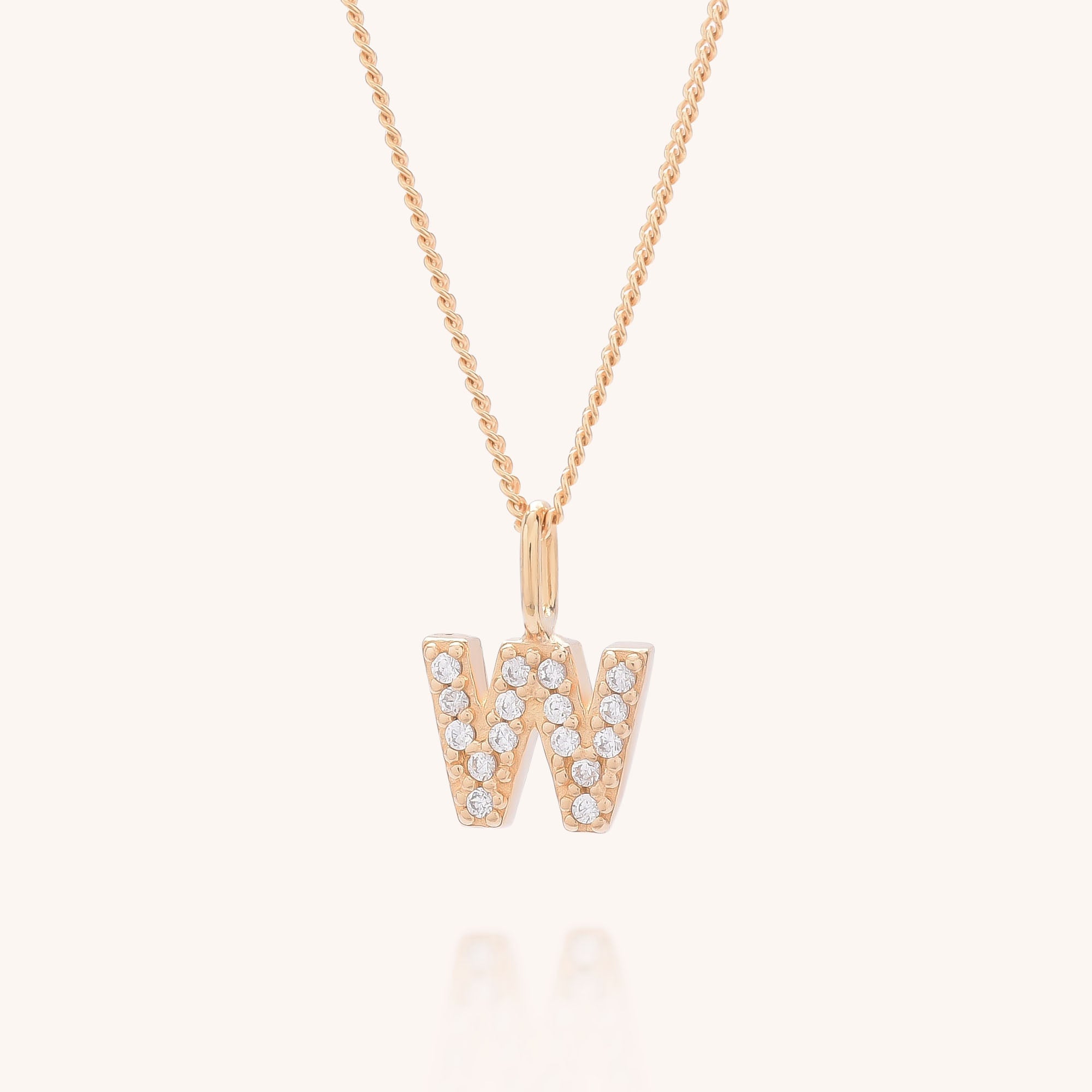 The Initial Sparkle Necklace showcases a gold W-shaped pendant adorned with sparkling cubic zirconia, set against a simple light backdrop.