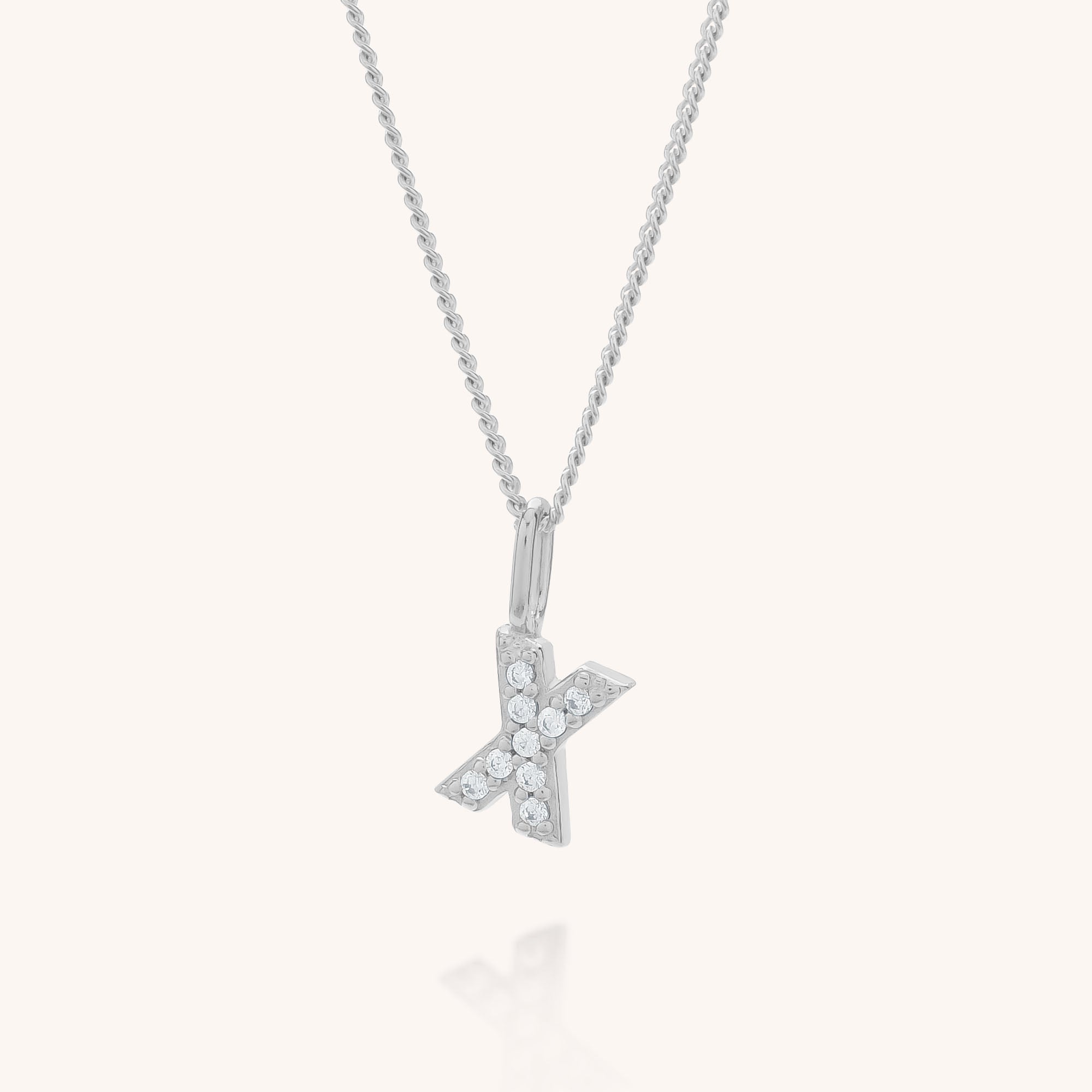 The Initial Sparkle Necklace features a silver pendant shaped like the letter K, embellished with sparkling cubic zirconia, showcased on a light neutral background.