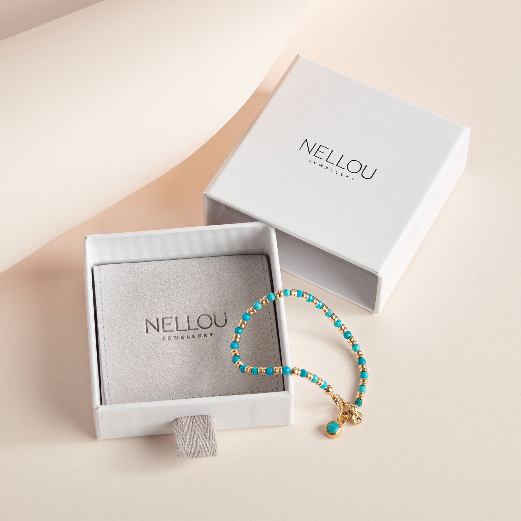 A Jewellery Box & Pouch with “NELLOU JEWELLERY” on the lid sits beside a turquoise and gold beaded bracelet, all set against a soft, neutral background—perfect for displaying your Nellou Jewellery.