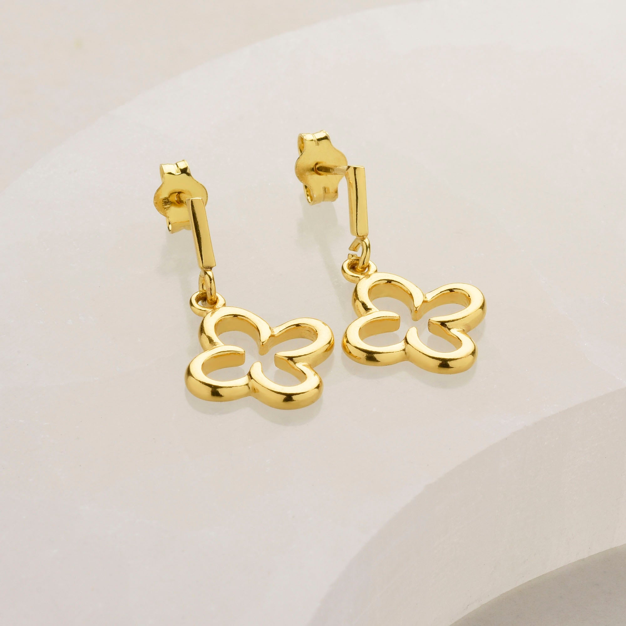 pair of gold eardrops in a clover design laid on a gemstone